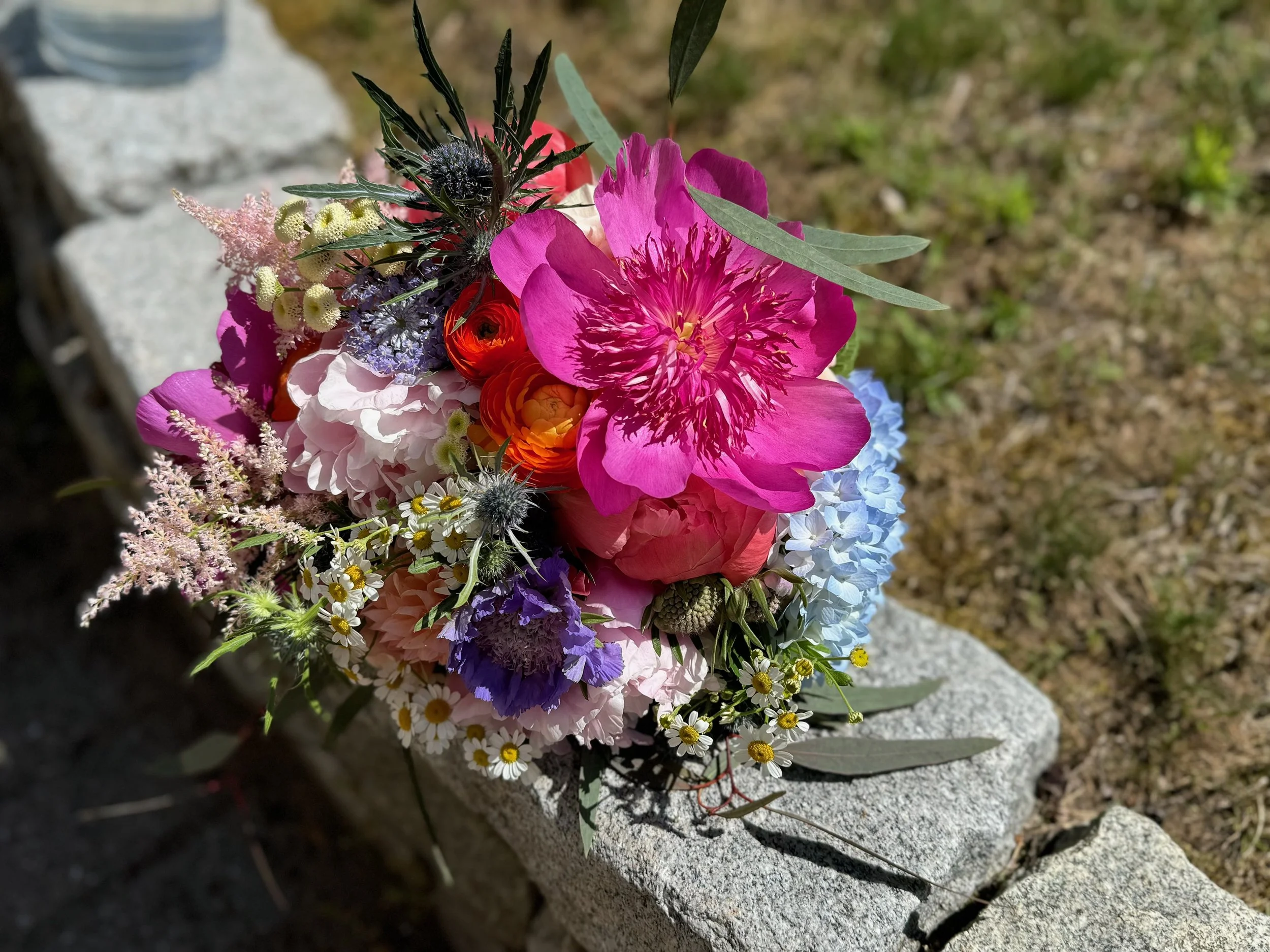 A colorful bouquet of flowers resting on a stone surface outdoors.