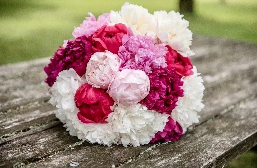 A bouquet of pink, white, and magenta peonies resting on a weathered wooden surface outdoors.