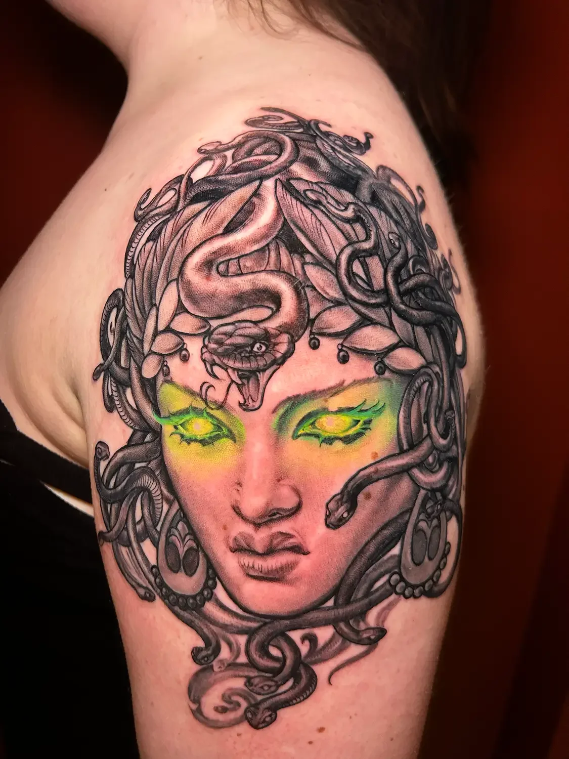 Blackwork arm tattoo of a Medusa's face with green eyes. Custom Design by RVA tattoo artist Fronkie.
