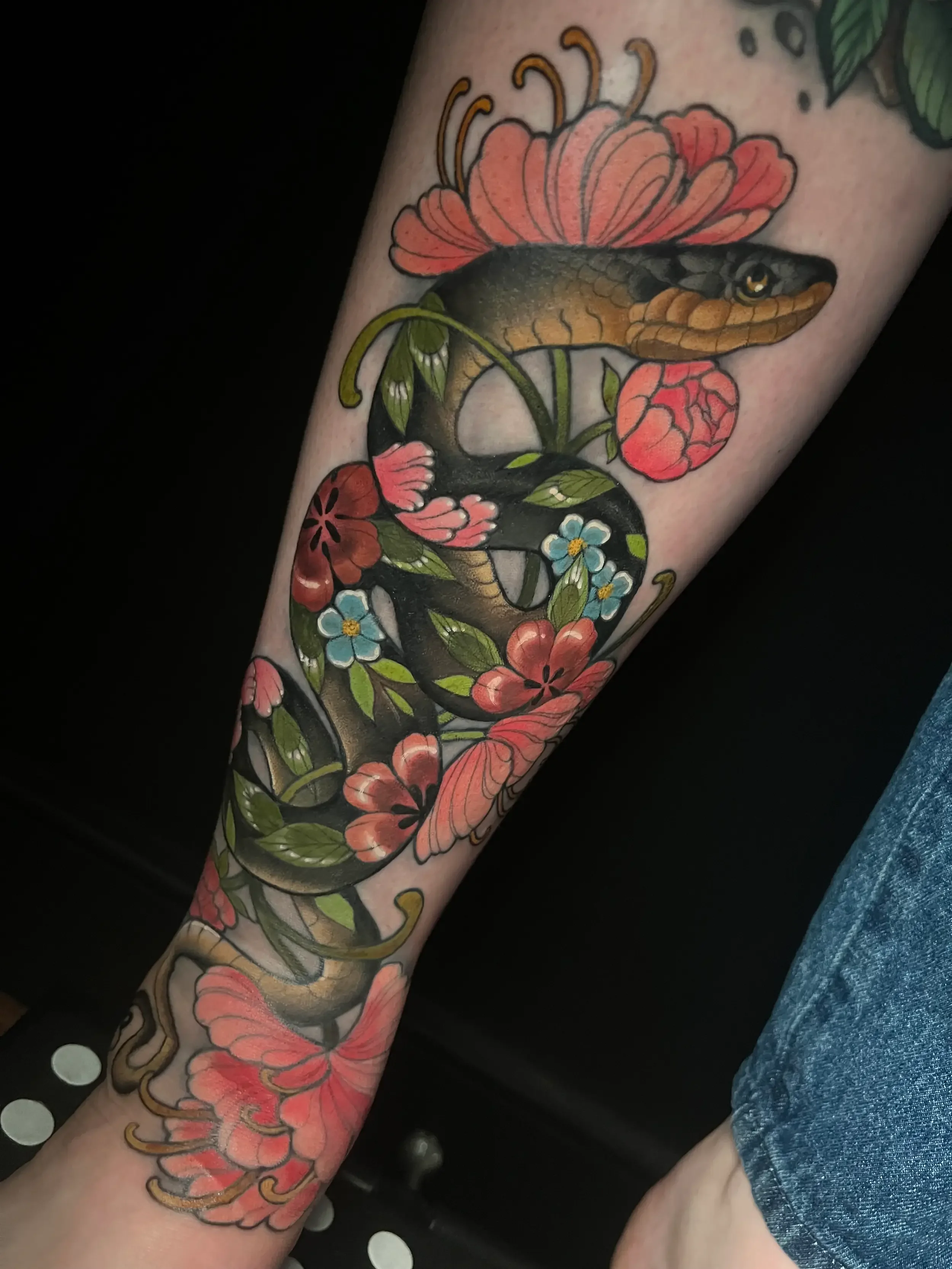 Neo-traditional color tattoo of a snake intertwined with colorful flowers on person's leg. Custom Design by female tattoo artist Dana Carlson in RVA.