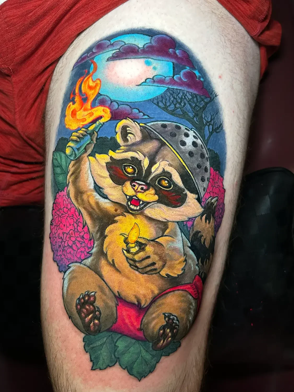Colorful tattoo of a raccoon sitting among pink and green foliage, with a full moon, purple clouds, a burning fire torch, and trees in the background. Custom Design by RVA tattoo artist Fronkie.