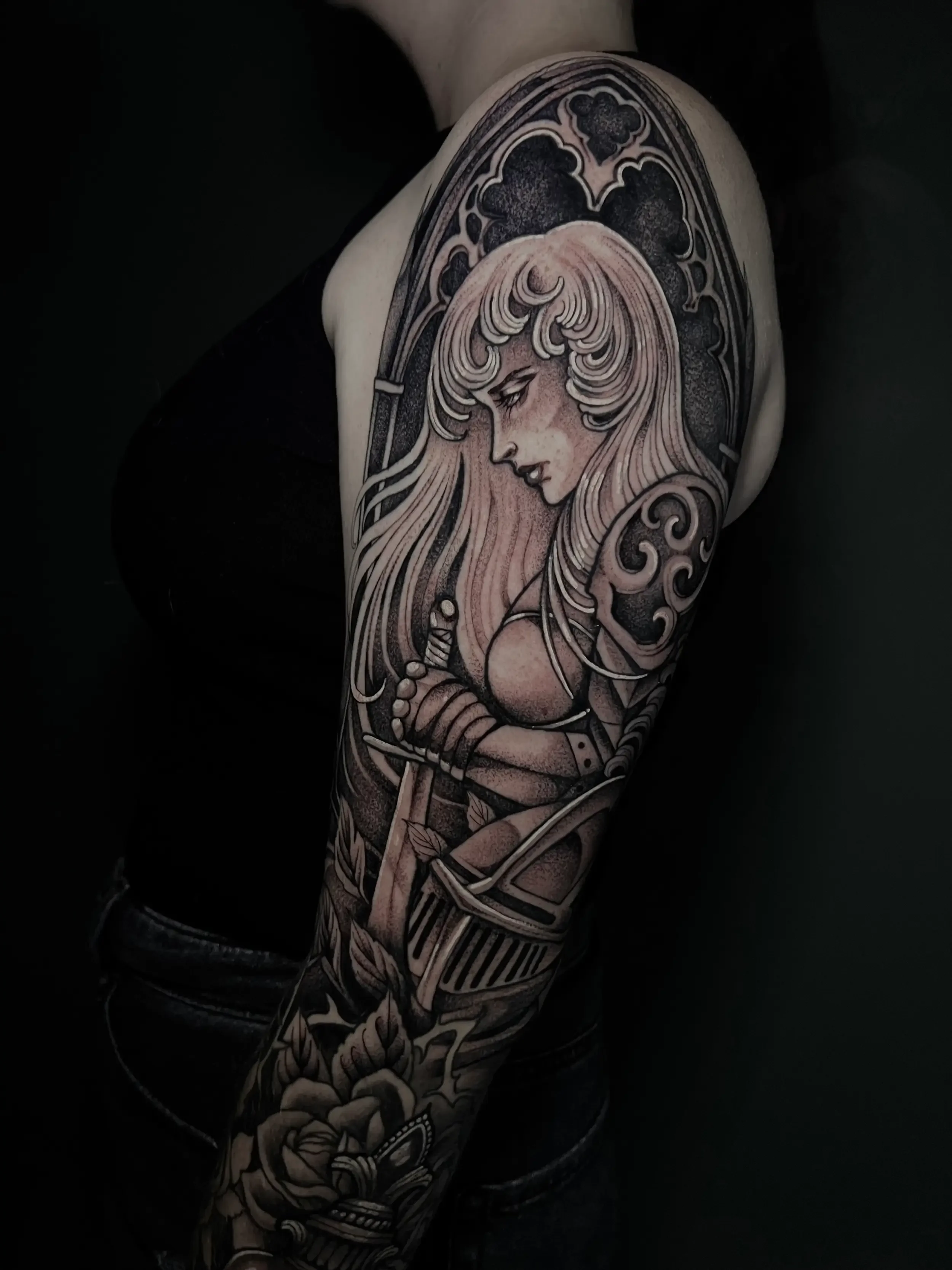 Black and gray fantasy tattoo of a female warrior with long hair and a sword on her arm, surrounded by decorative patterns on upper arm. Done by female tattoo artist Dana Carlson in Virginia.