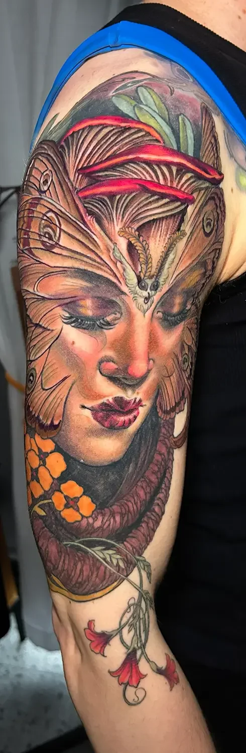 Color fantasy tattoo of a woman's face with butterfly wings covering her head, surrounded by orange flowers and decorative leafy elements. Custom Design by RVA tattoo artist Fronkie.