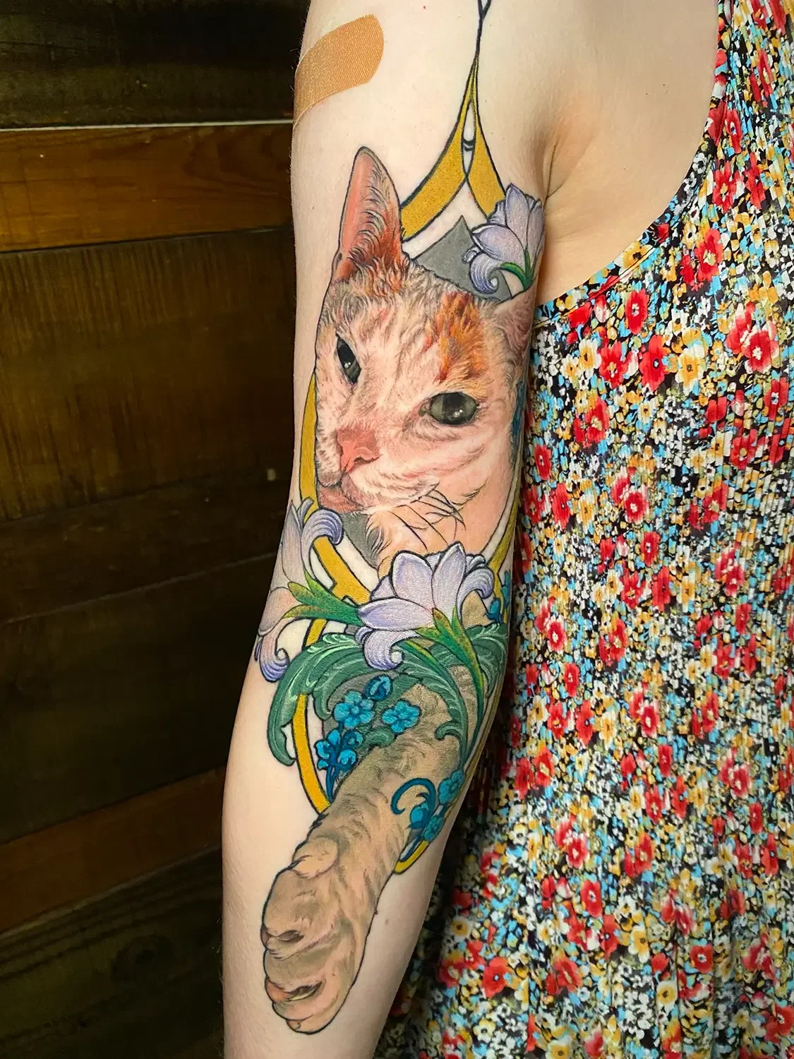 Colorful pet portrait tattoo of a cat's face surrounded by flowers on a person's upper arm. Custom Design by RVA tattoo artist Fronkie.