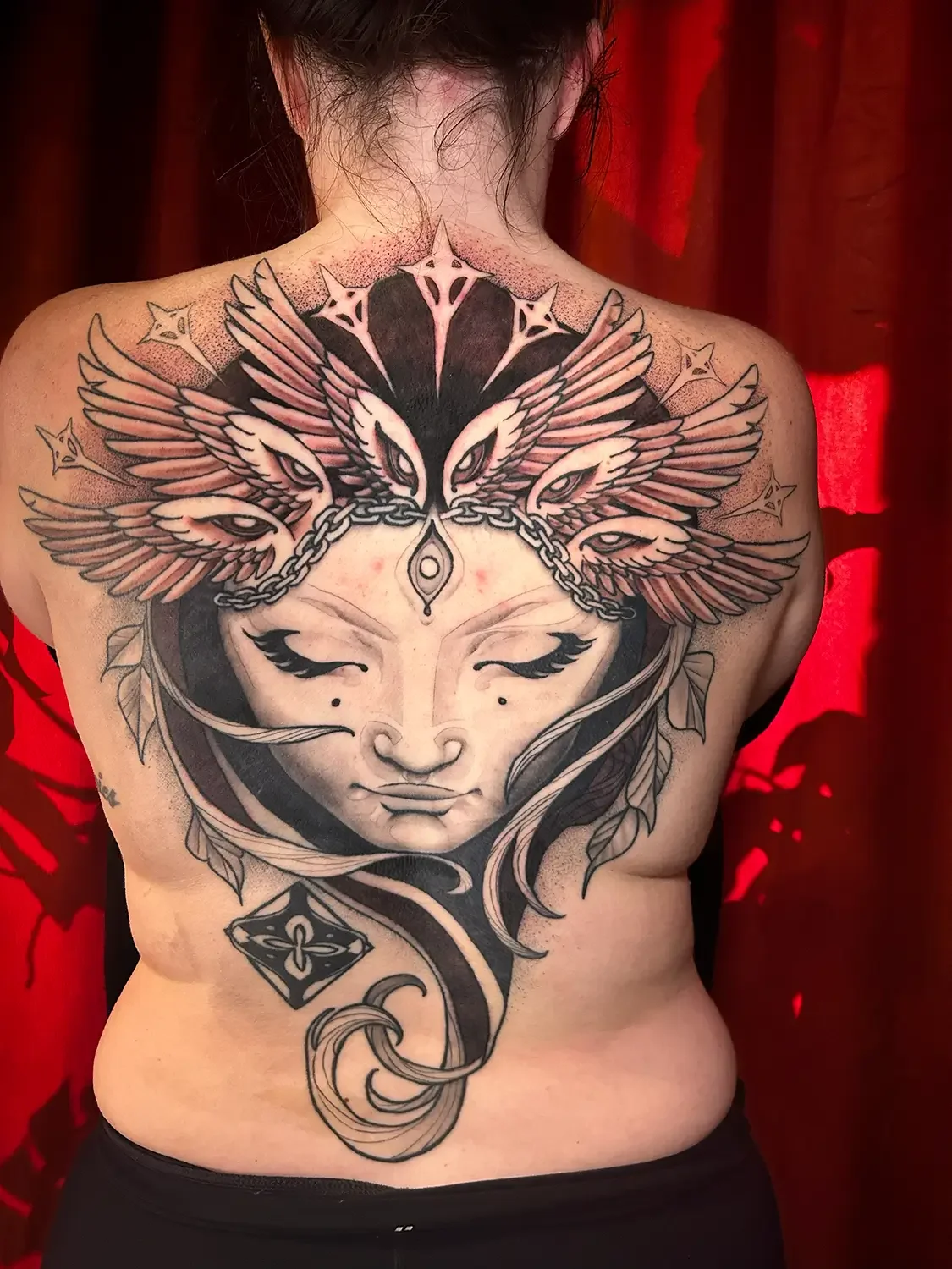 Tattoo of a stylized woman's face with closed eyes, leaves, wings, chains, and decorative elements on the back. Custom Design by RVA tattoo artist Fronkie.