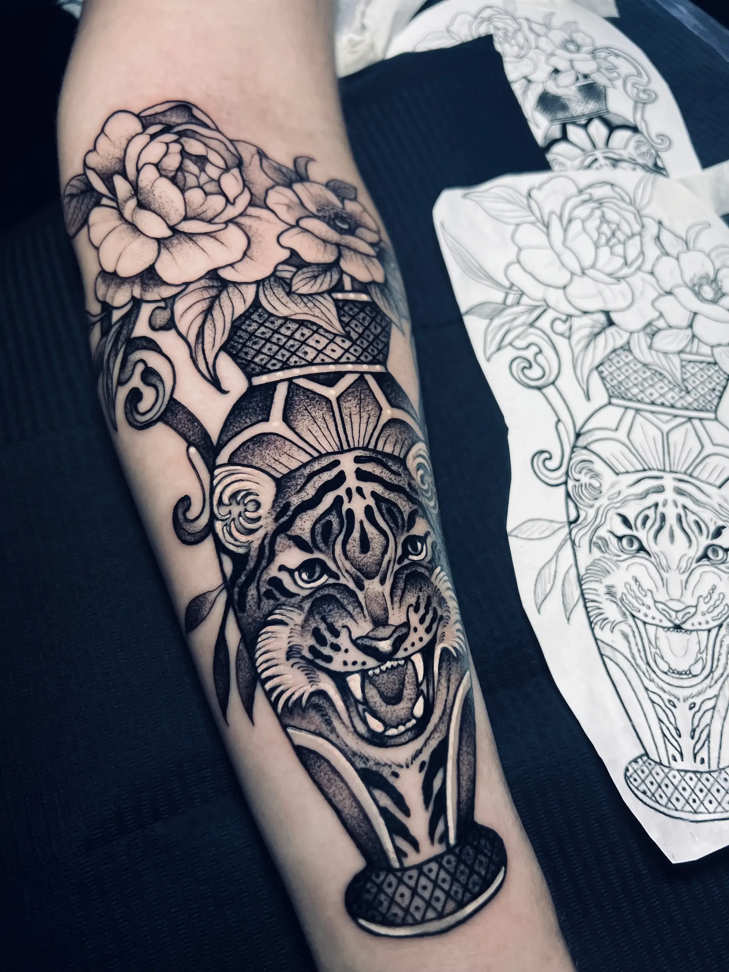 Black and gray tattoo of a tiger's head on a decorative vase with large flowers and leaves, on a person's arm. Done by female tattoo artist Dana Carlson in RVA.