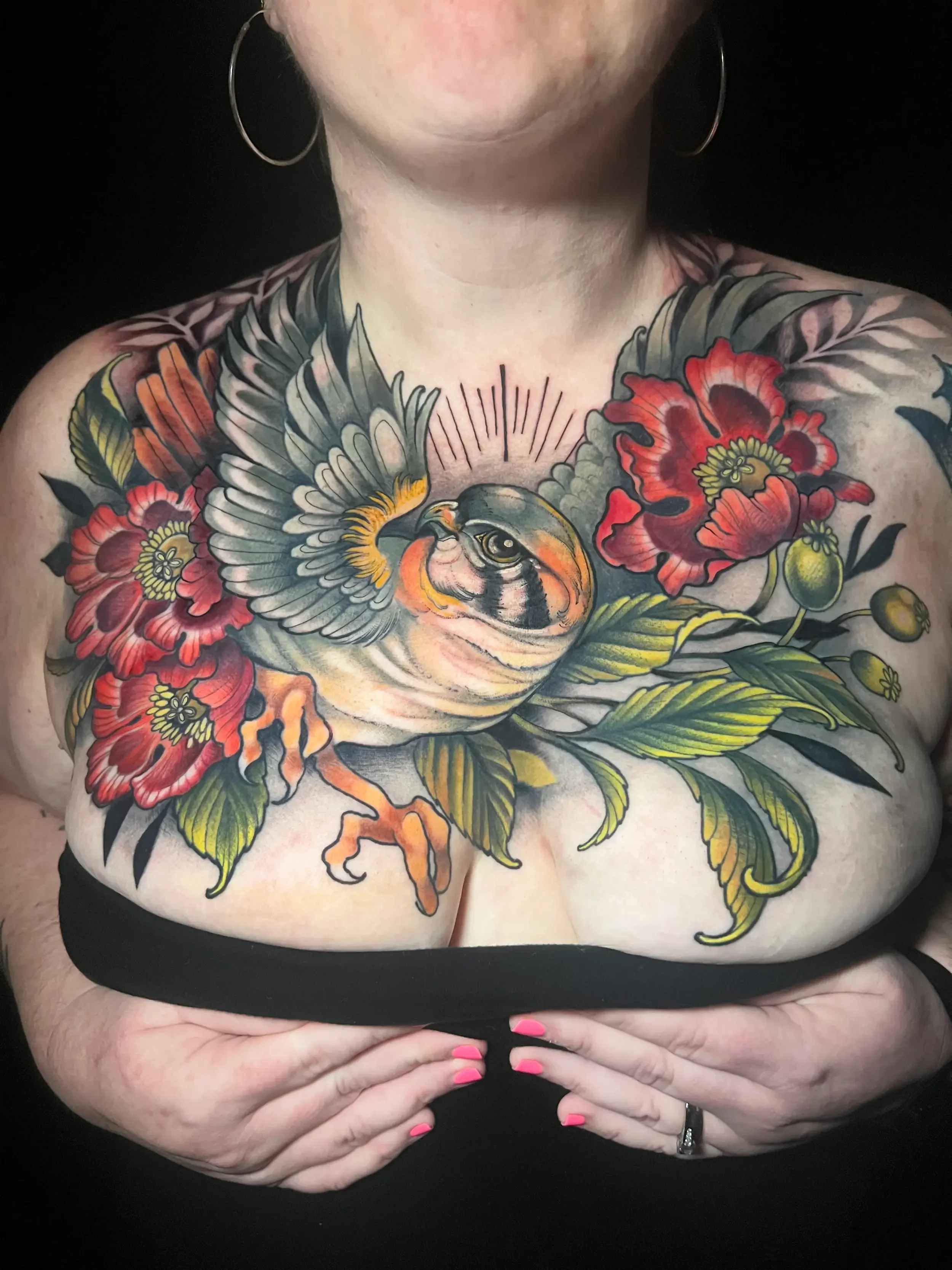Colorful neo-trad chest tattoo of a falcon surrounded by red flowers and green leaves. Custom Design by female tattoo artist Dana Carlson in Virginia Beach.