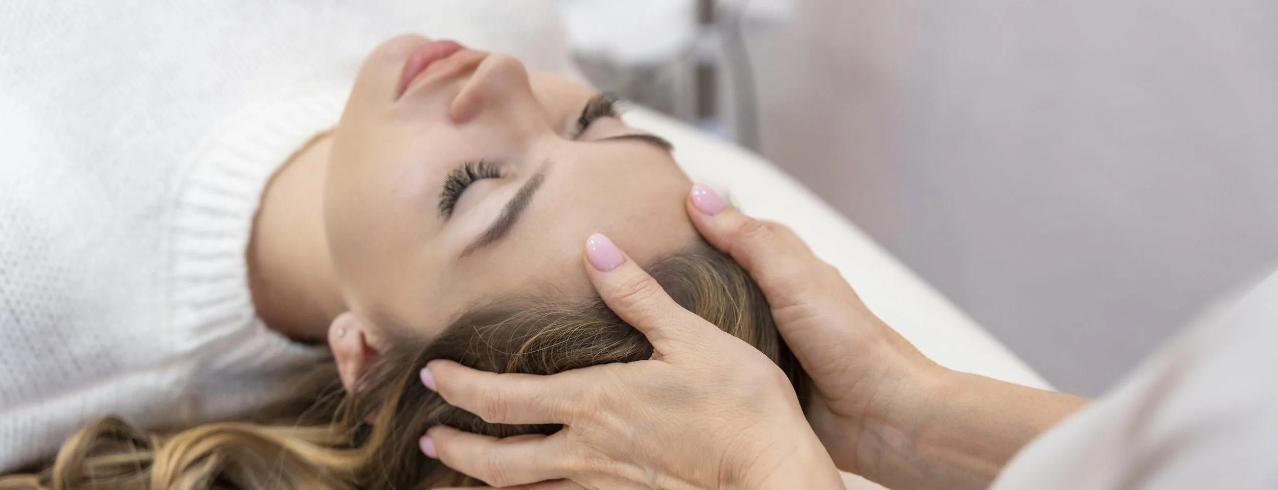 A woman receiving an energy treatment with a practitioner's hands on her temples.