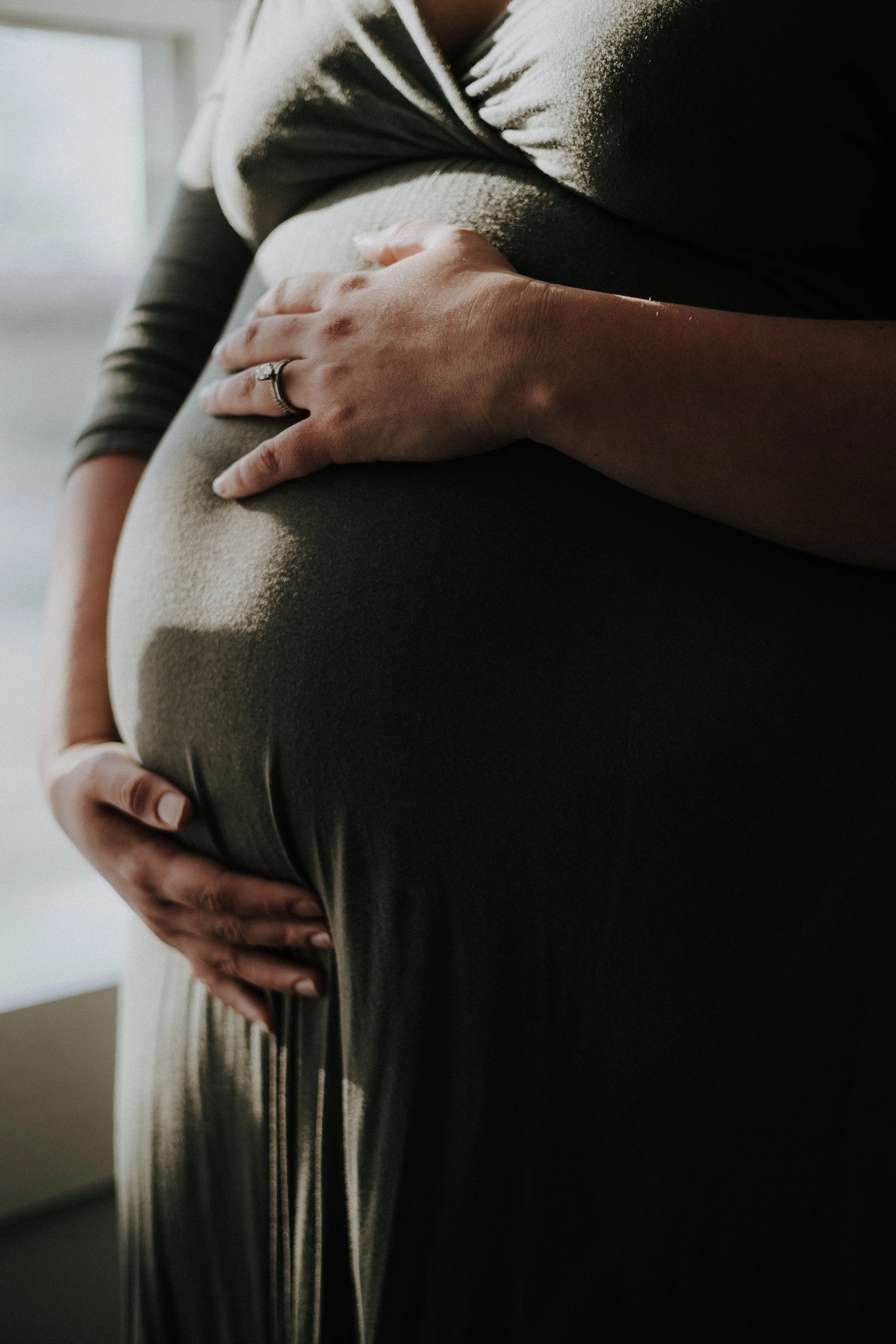Close-up of a pregnant woman holding her twin baby bump in a soft, natural light at their home in Norwalk ohio