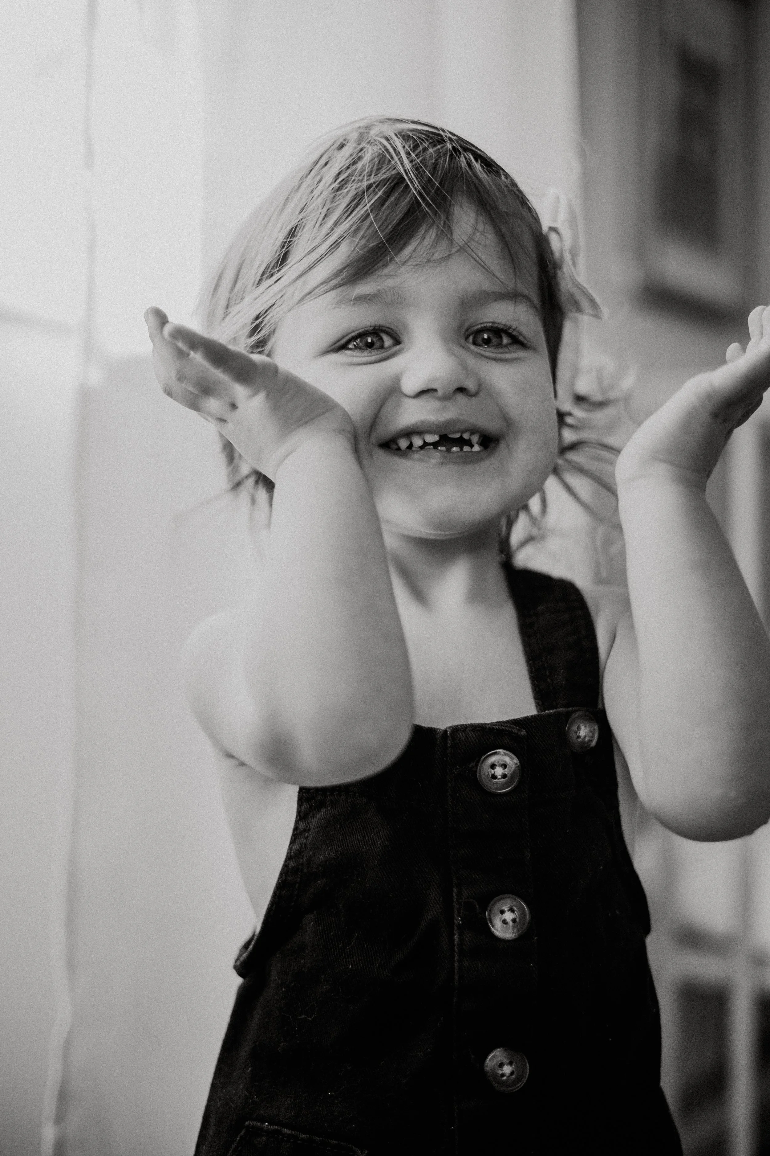 a Calvin Klein inspired Black-and-white photo of a young girl smiling with a missing tooth, playful pose, hands near her face, in casual clothing.