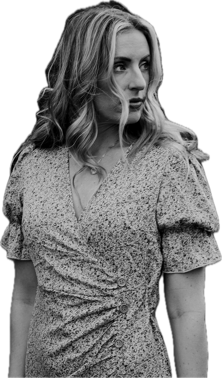 Black and white photograph of a woman with wavy, shoulder-length hair looking to her left, wearing a patterned dress with buttons and a necklace.