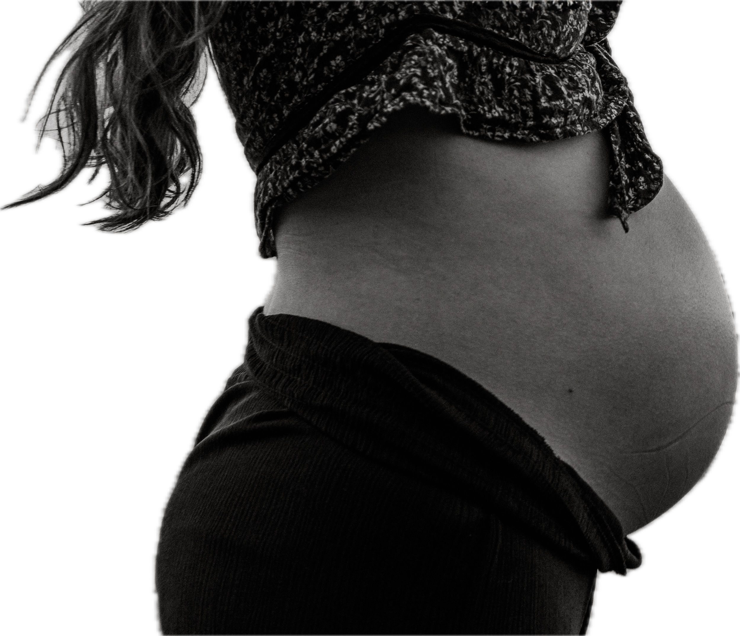Close-up of a pregnant woman's belly, wearing a cropped patterned top and black pants at a beach in huron ohio