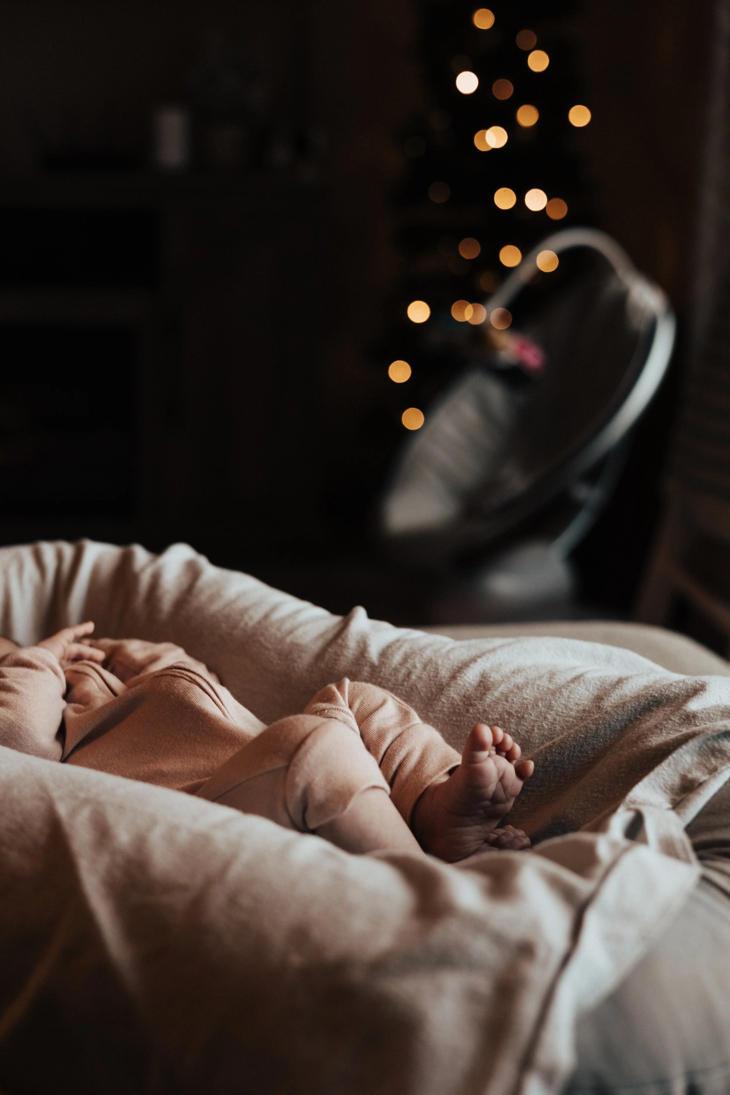 A newborn baby lying in a cozy chair, with a decorated Christmas tree with blurred lights in the background. in home session in Norwalk ohio