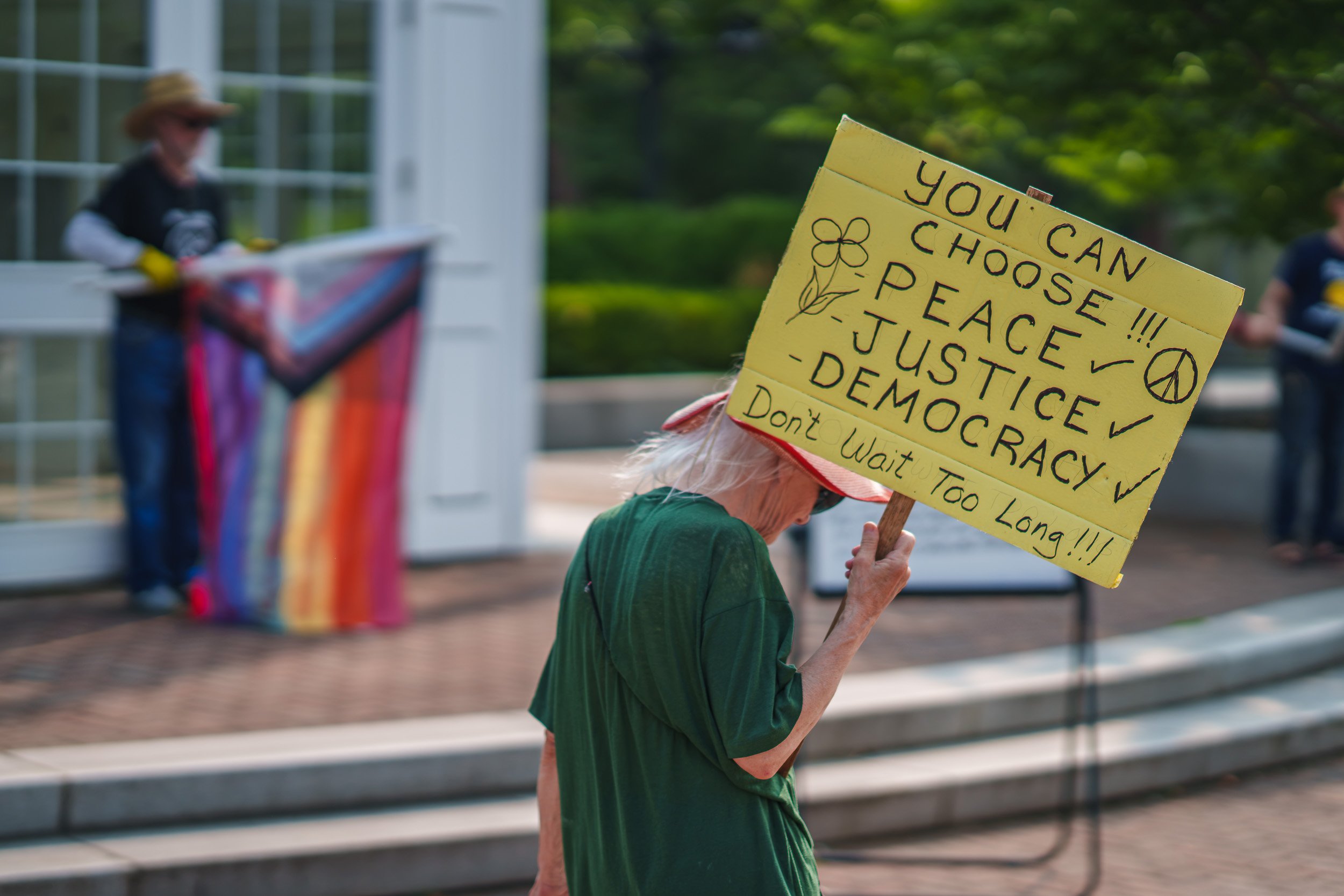 A participant of the July, 14 2026 No Kings protest holds a sign towards traffic while another waves a pride flag in Park Square, in the center of Westfield, Ma.