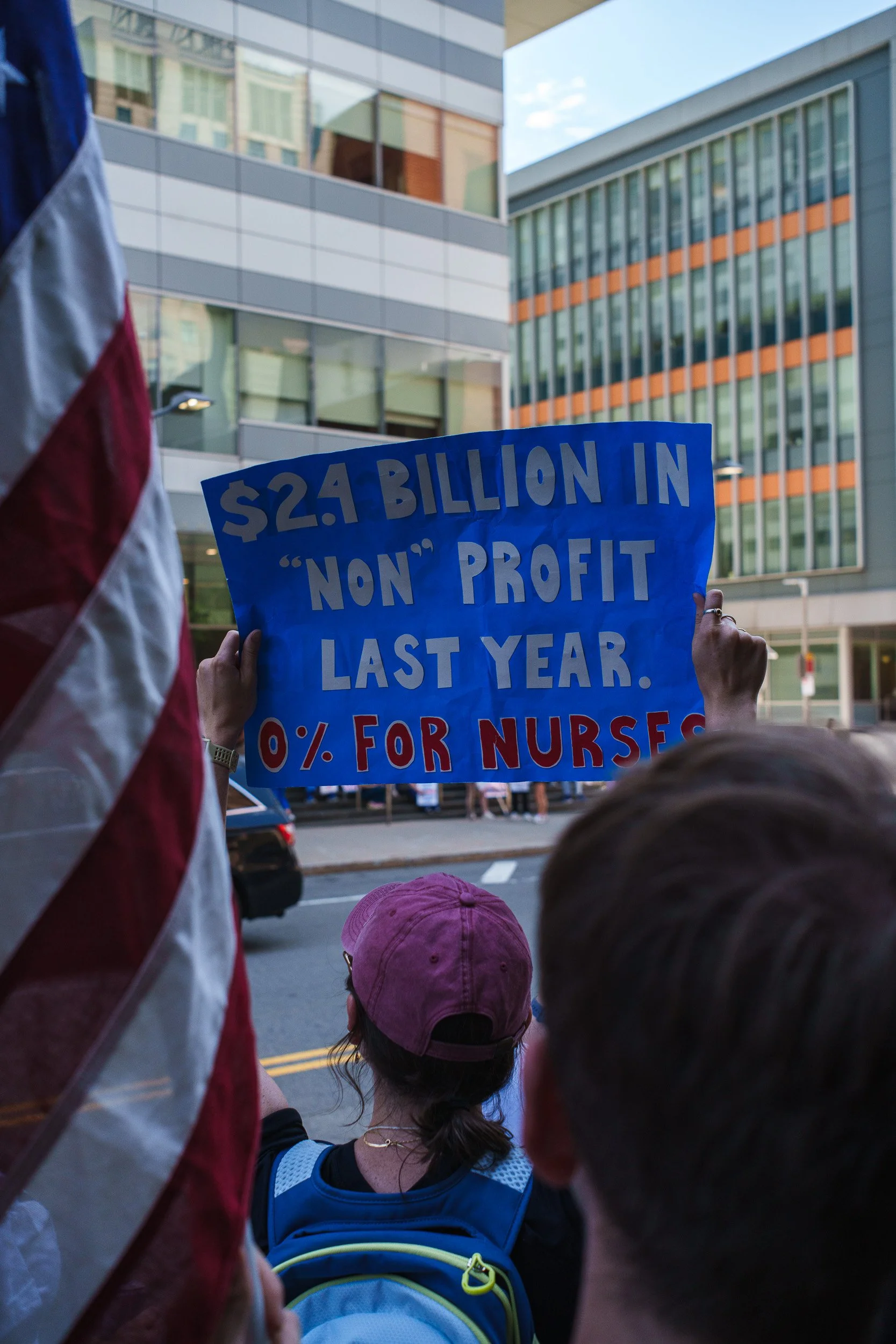A protester holds a sign in front of Mass General Brigham Hospital in Boston on July 9, 2026.  The protesters, mostly nurses employed by Mass General Bingham, engaged in a mass walk-out on July 8, 2026 in an effort to increase compensation and patien