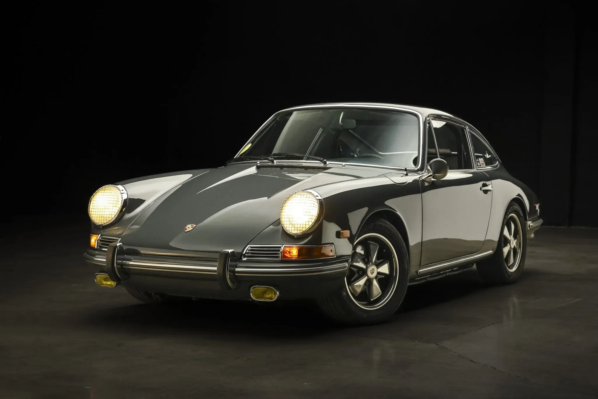 A classic Porsche 911 sports car with black and silver coloring, round headlights, and vintage styling parked on a dark surface.