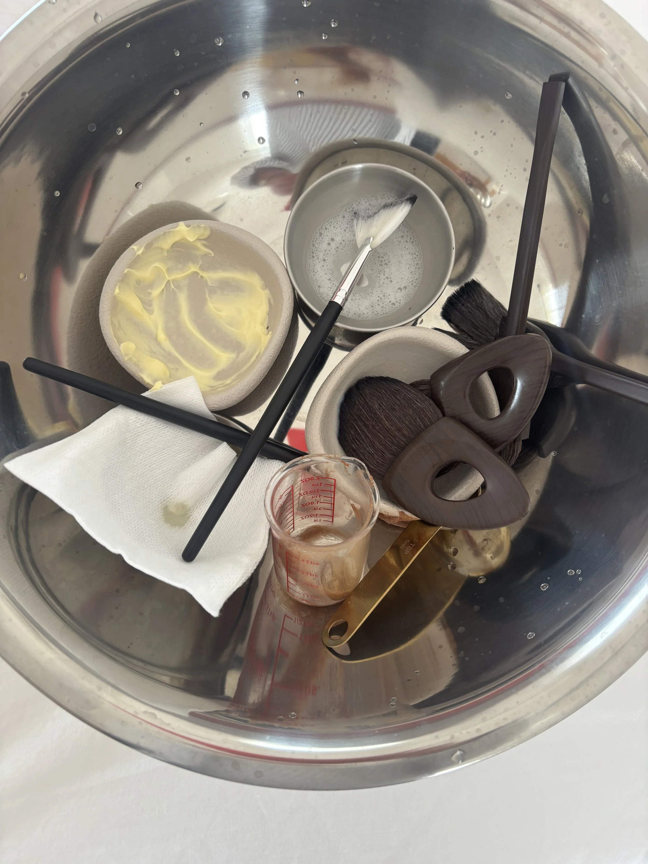 The interior of a stainless steel household appliance, likely a washing machine or dryer, containing a brush, a small container of liquid, a paper towel, and some other cleaning tools.