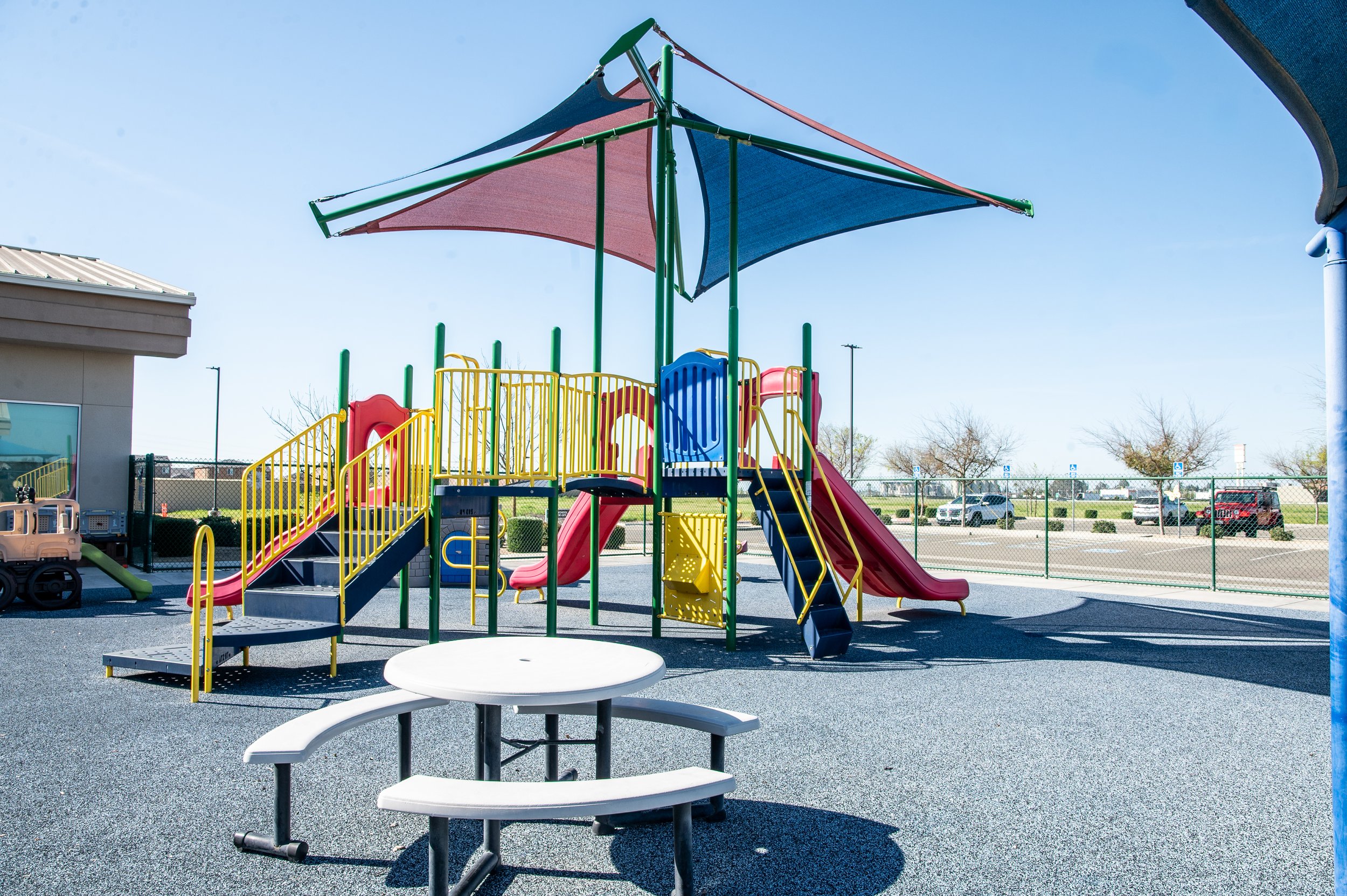 Colorful playground with slides, climbing structures, shaded canopy, and picnic table in an outdoor park area.