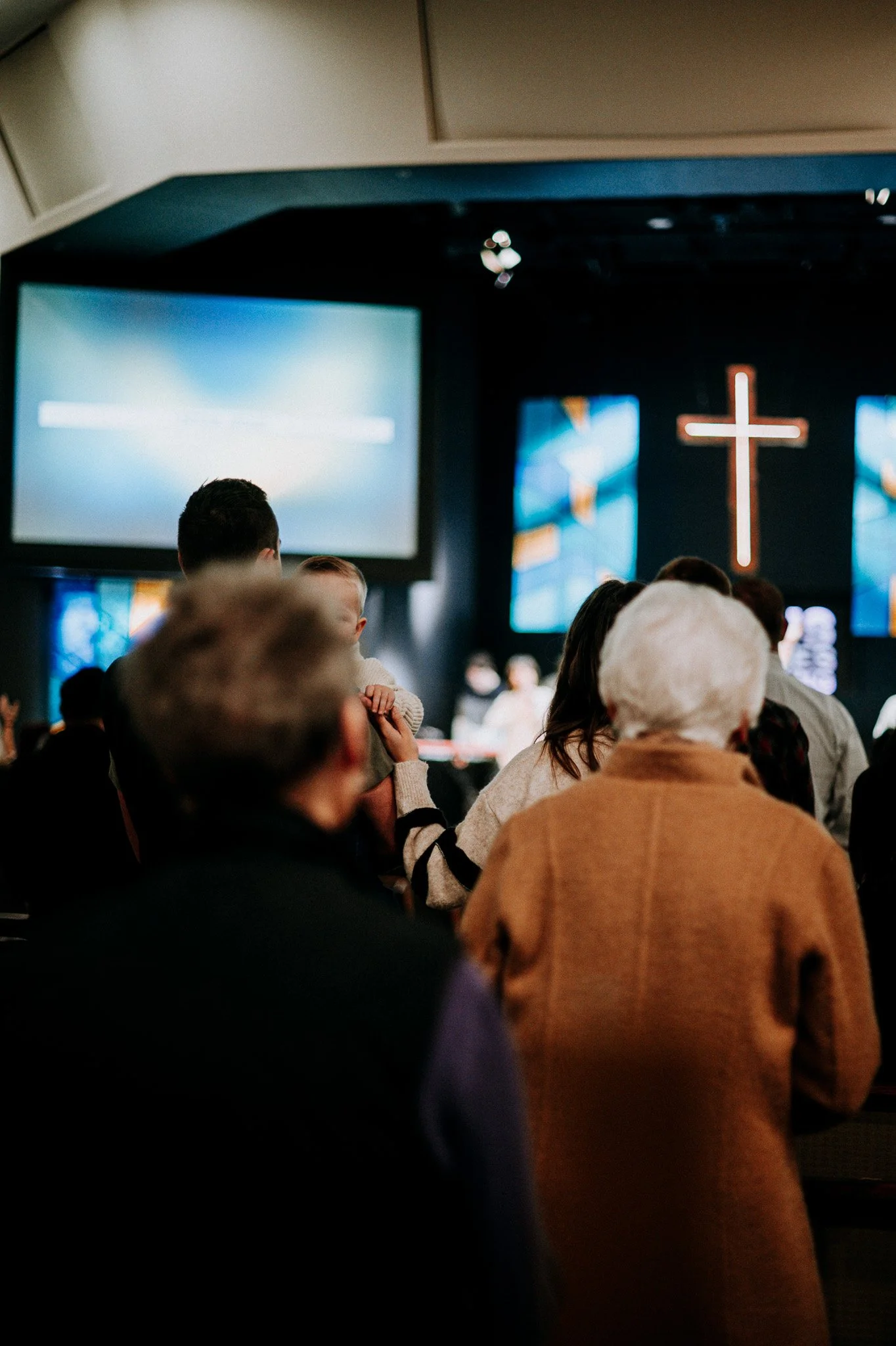 People attending a church service with a prominent illuminated cross on the stage background.