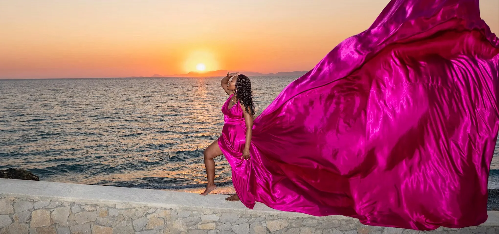 Beautiful lady is posing in a pink flying dress at a Rhodian sunset.