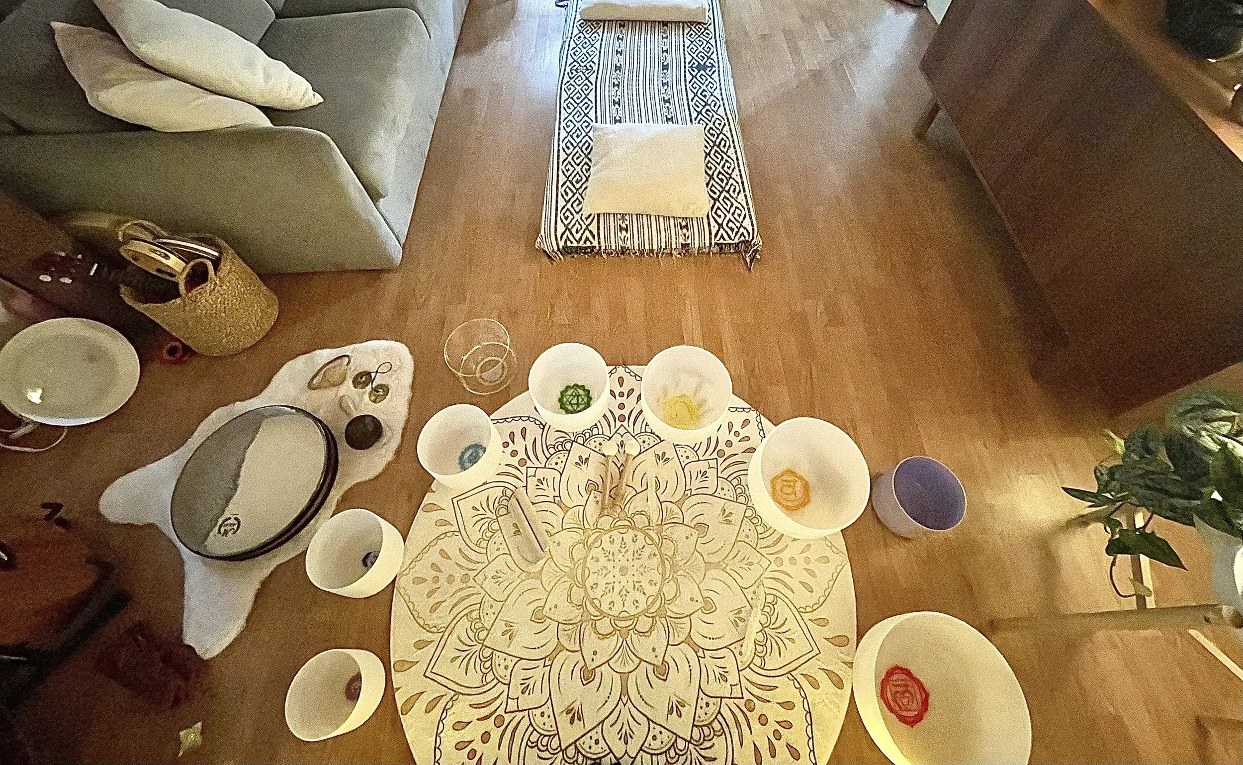 Table with decorative cloth, bowls, and plates, set for a meal, in a living room with a sofa, pillows, and wooden floor.