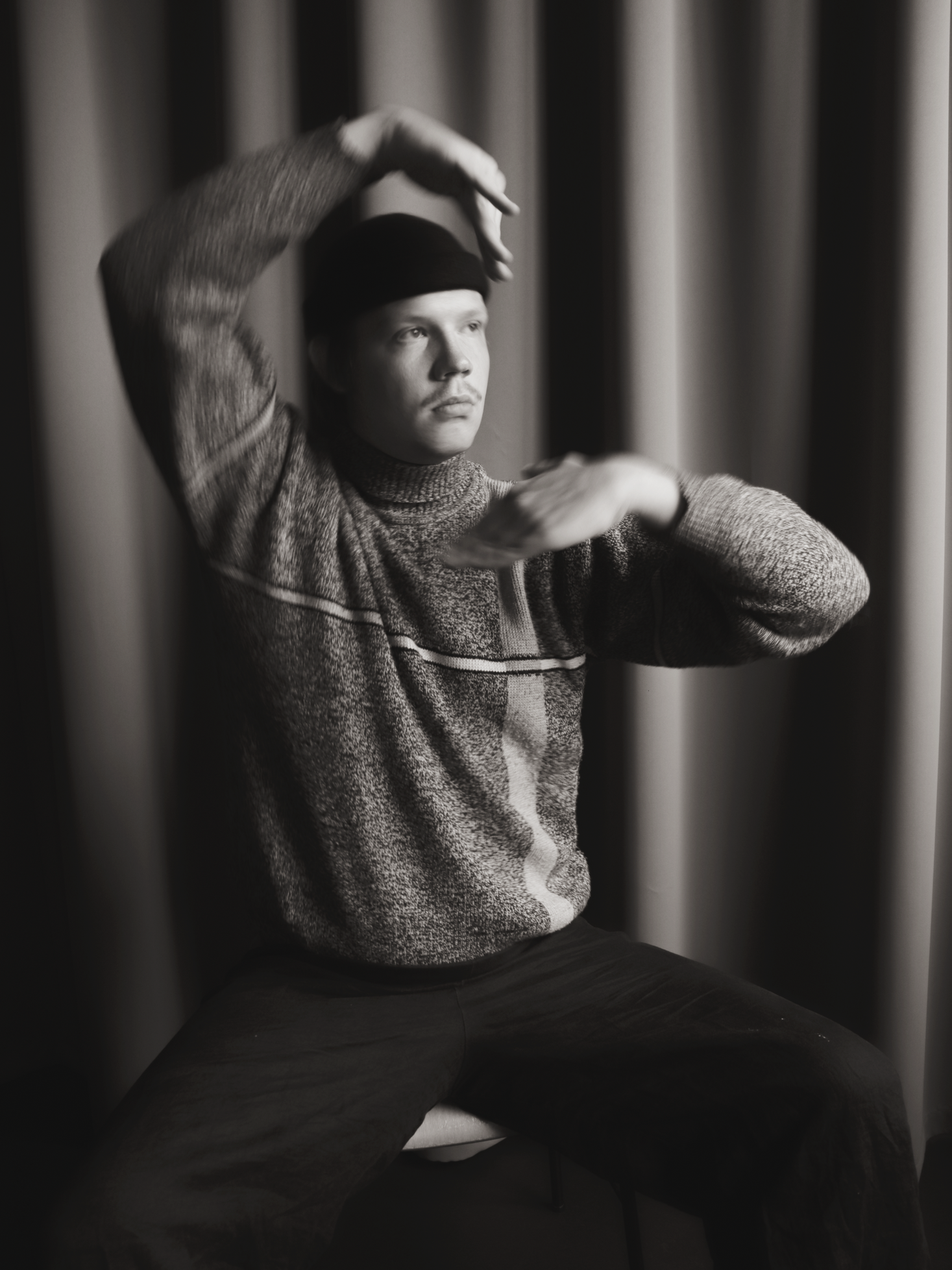 Schwarze und weiße Fotos eines Jungen, der auf einem Stuhl sitzt, mit einer mützenähnlichen Kopfbedeckung und einem dicken Pullover, der die Aufmerksamkeit auf das Gesicht lenkt.