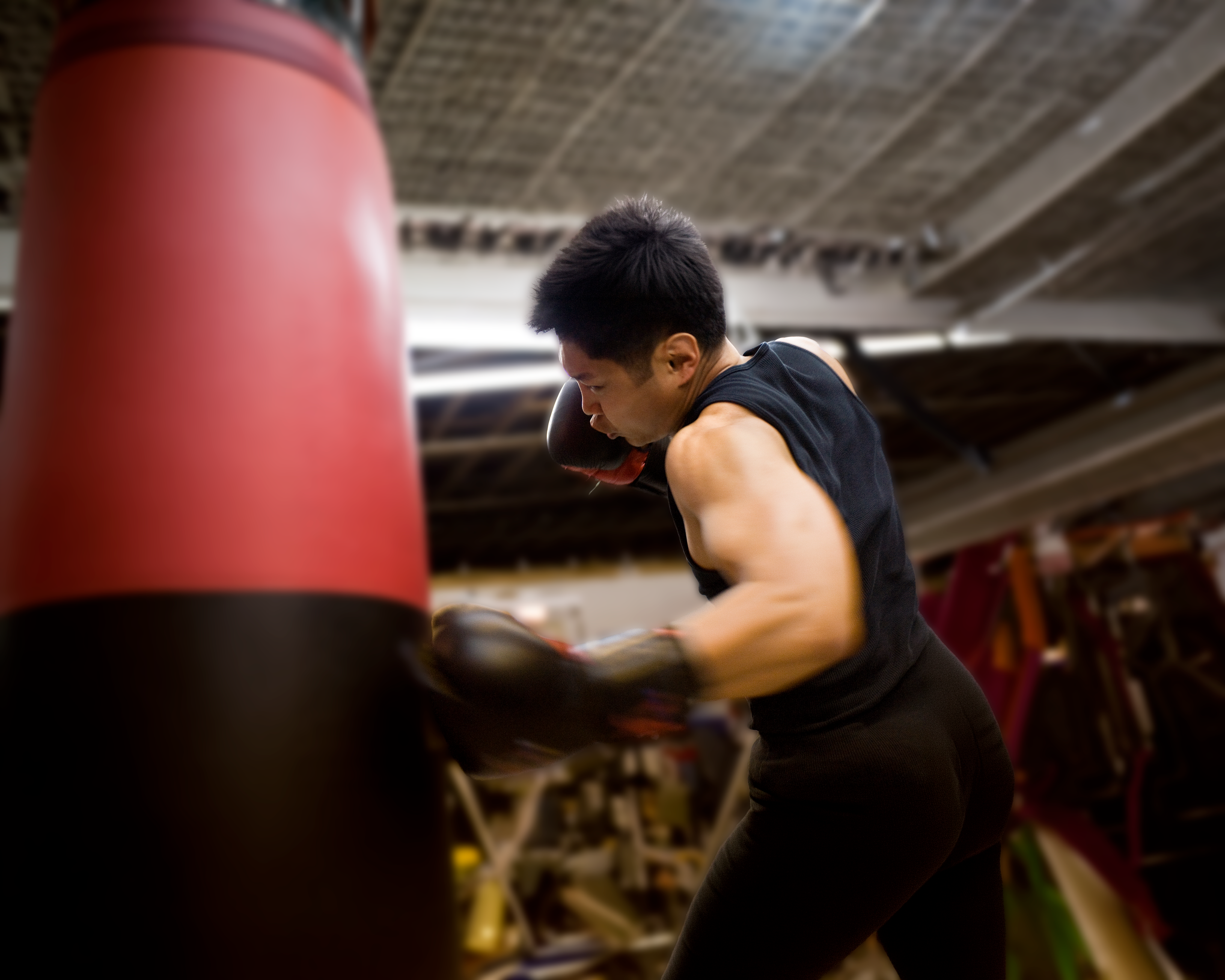 A person practicing boxing with a punching bag in a gym, wearing black workout clothes and boxing gloves.