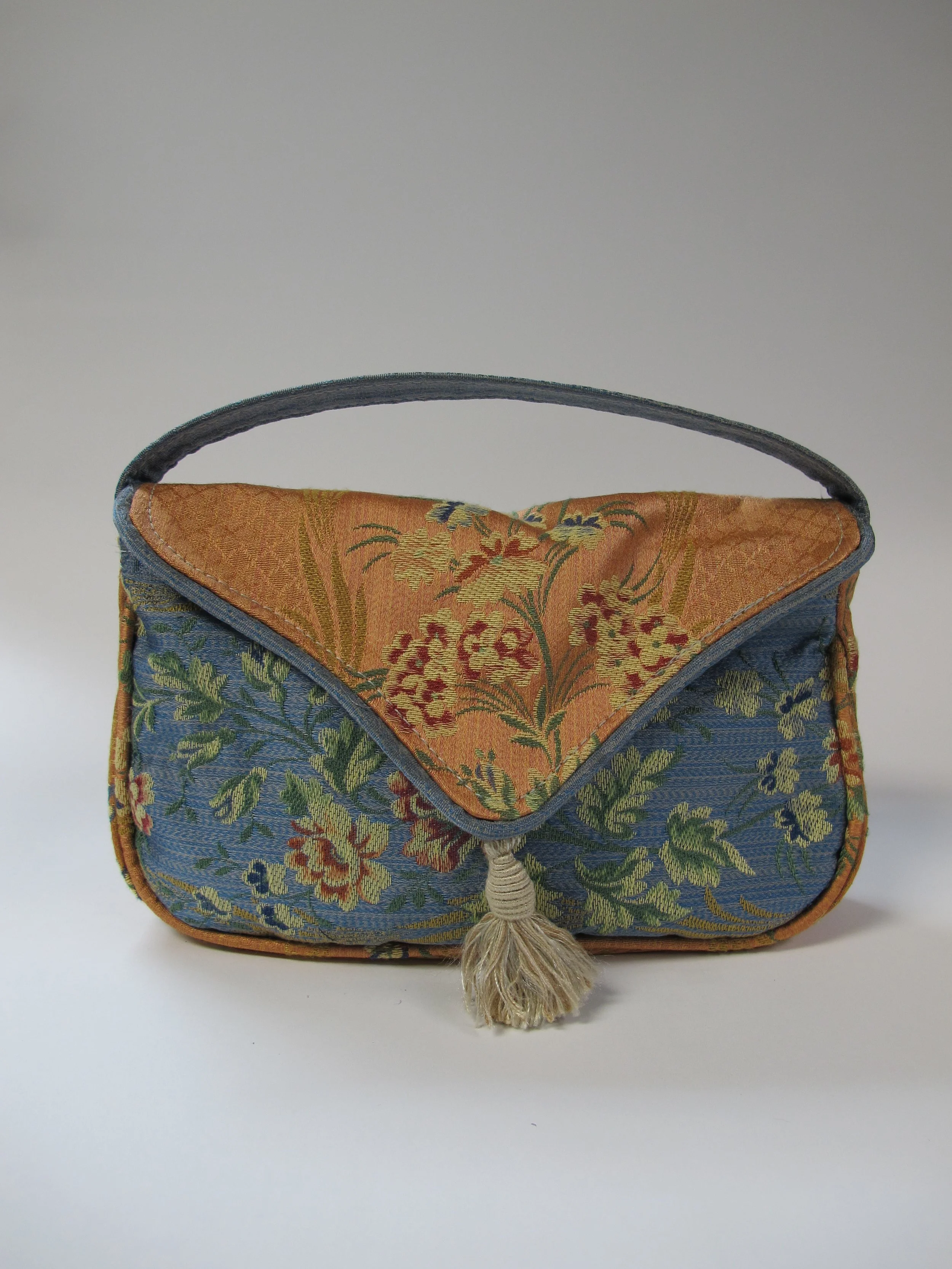 A small ornate fabric purse with floral tapestry design, featuring orange, blue, and green colors and a tassel on the front.
