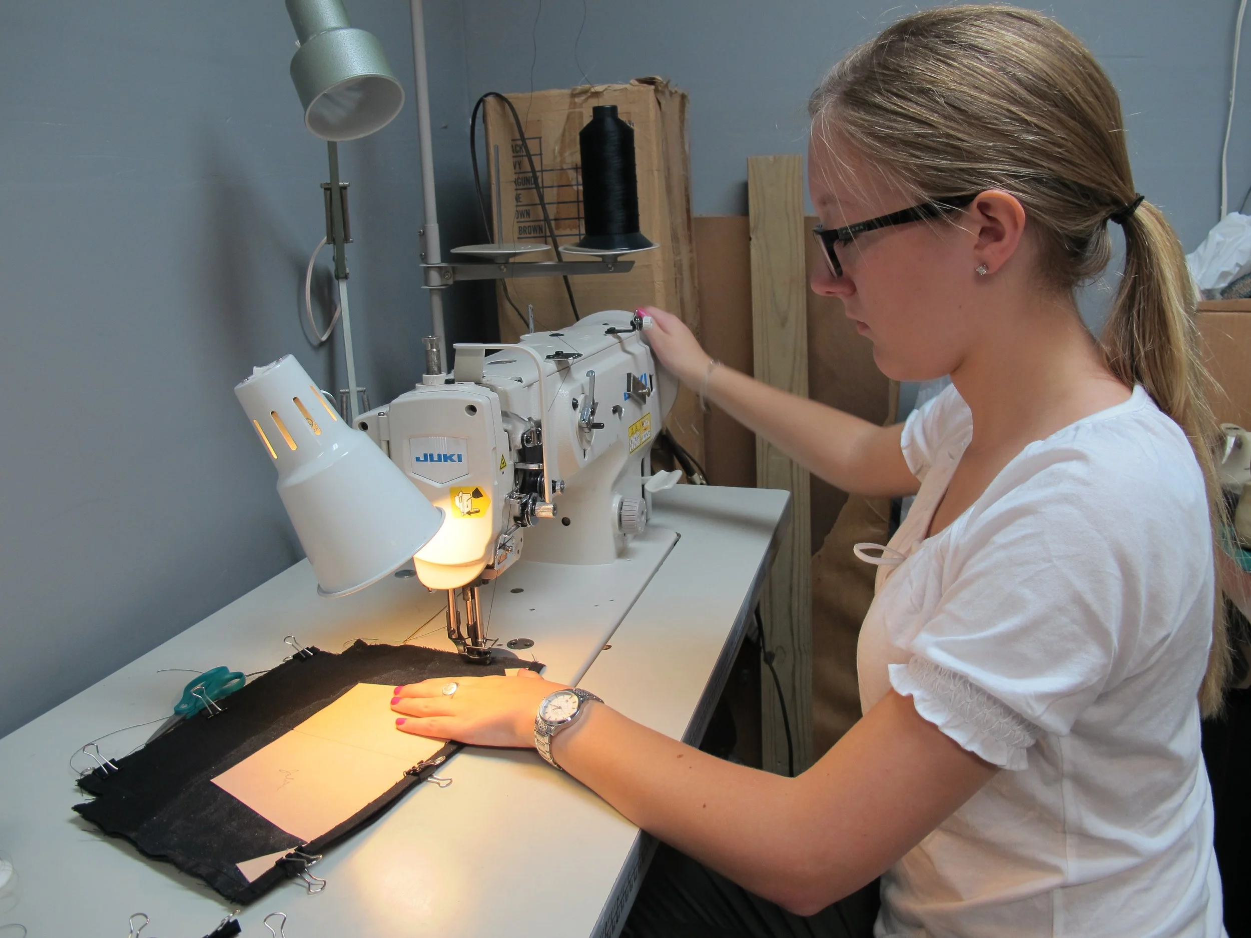 A woman sewing fabric using a Juki industrial sewing machine in a workshop.