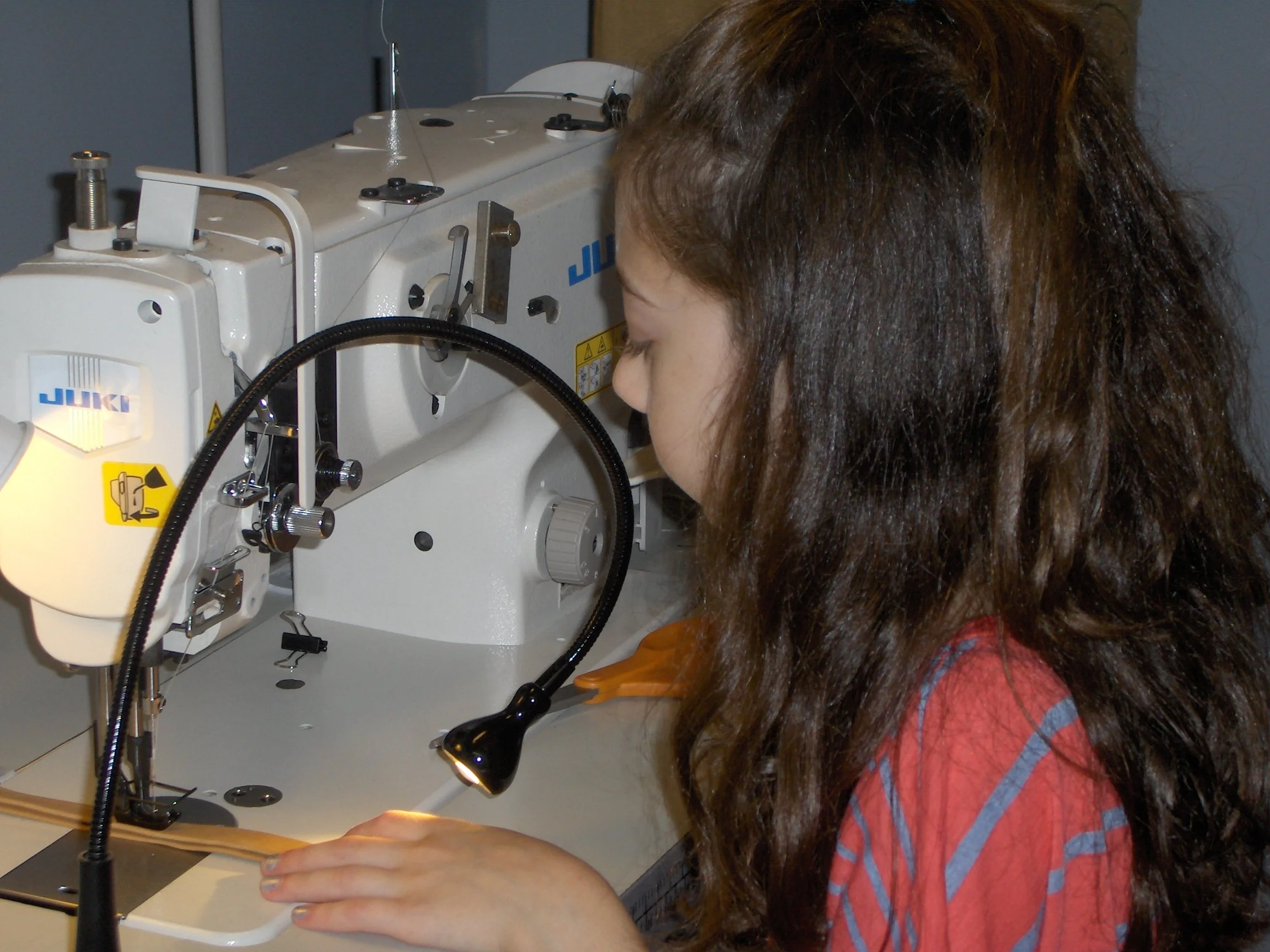 Young girl sewing fabric with a white industrial sewing machine.
