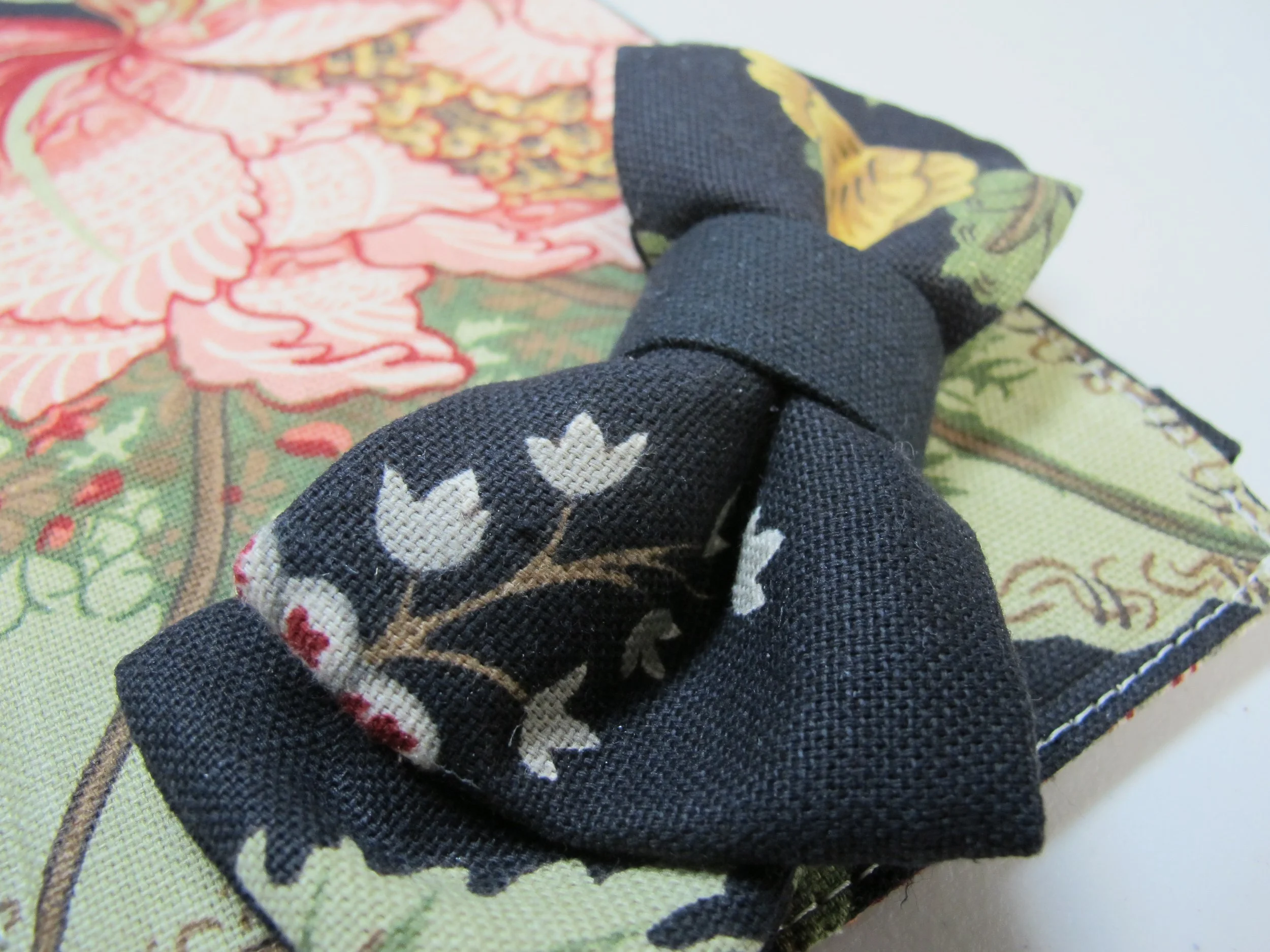 A floral patterned fabric with pink, green, and yellow designs, and a black fabric bow with white tulip and red flower embroidery, placed on top.