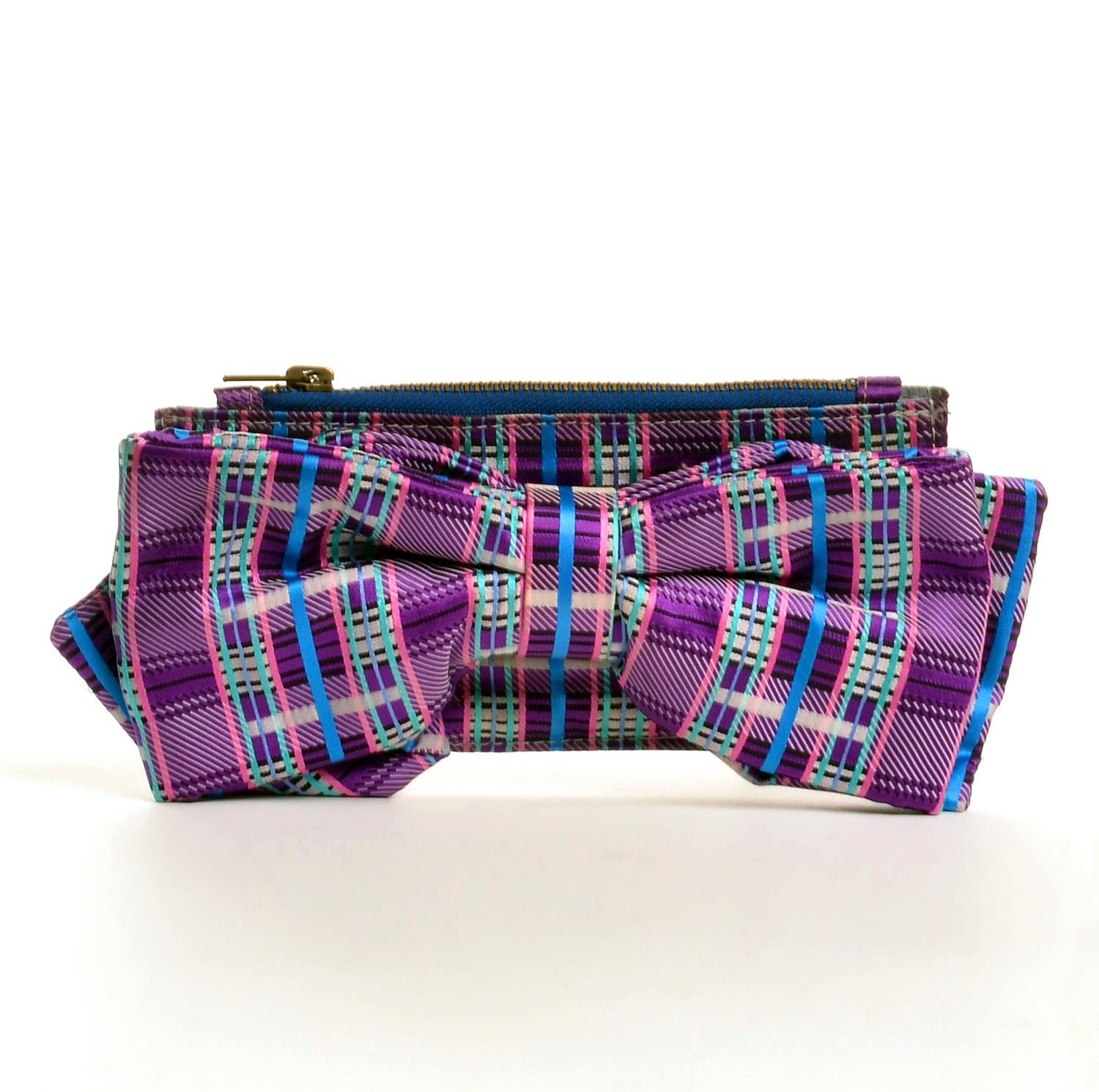 A colorful clutch purse with a large bow, featuring a pink, purple, blue, and green plaid pattern, against a plain white background.