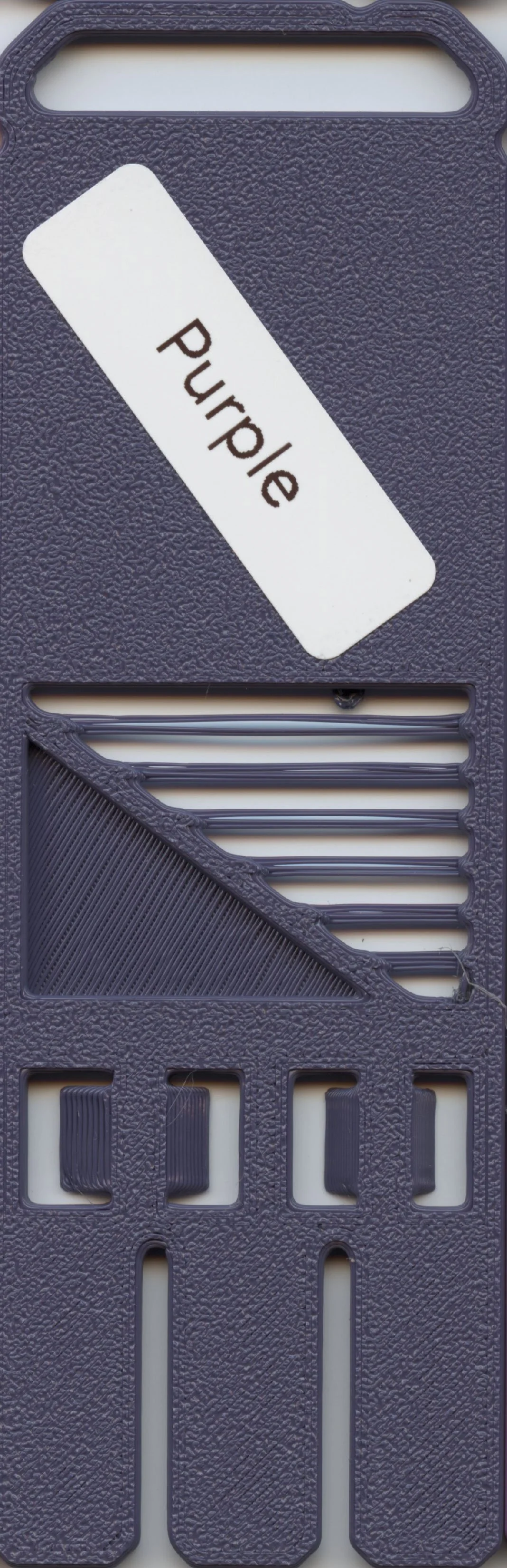 A black plastic object with multiple horizontal and vertical slots and a white label with the word 'Purple' on it.