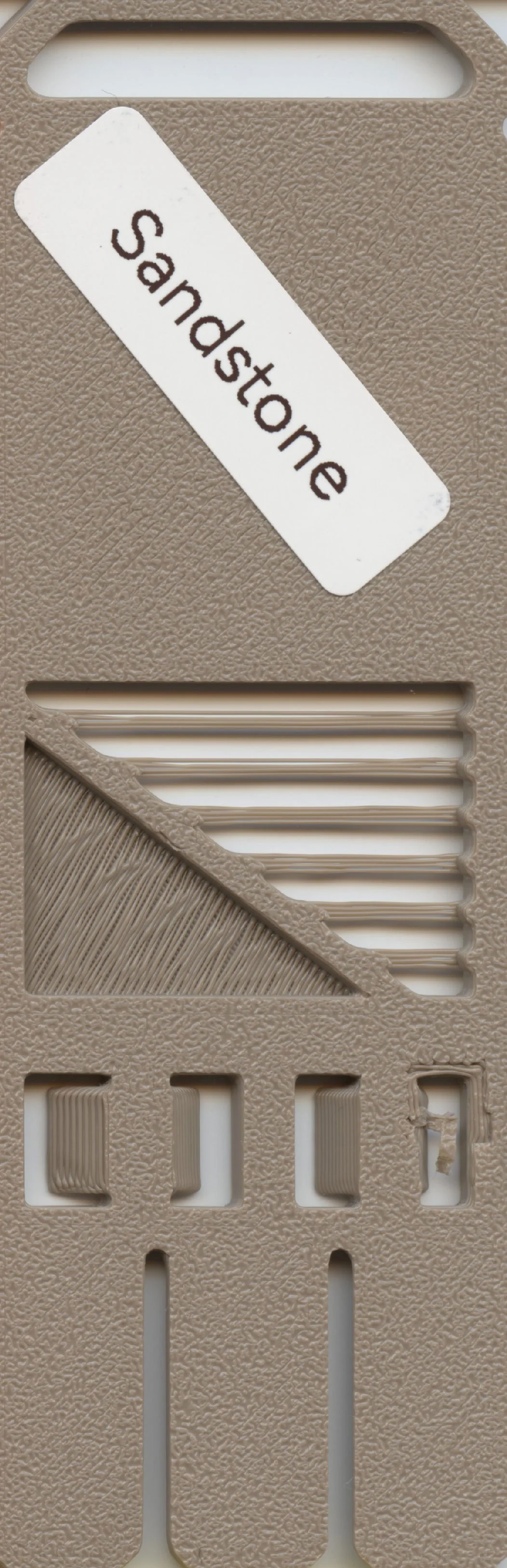 A beige plastic object with a white label reading 'Sandstone' and various textured grooves and slots.