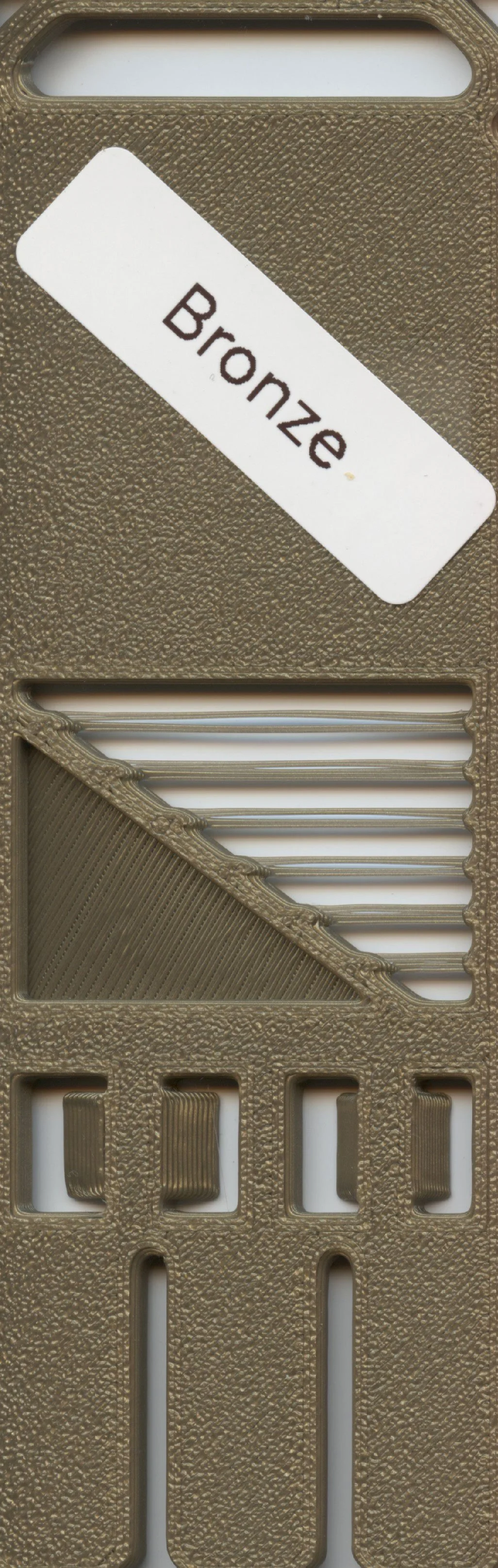 Close-up of a microneedle patch packaging with a white label that reads "Bronze" and a textured gold-colored plastic cover with multiple rectangular and diagonal openings.