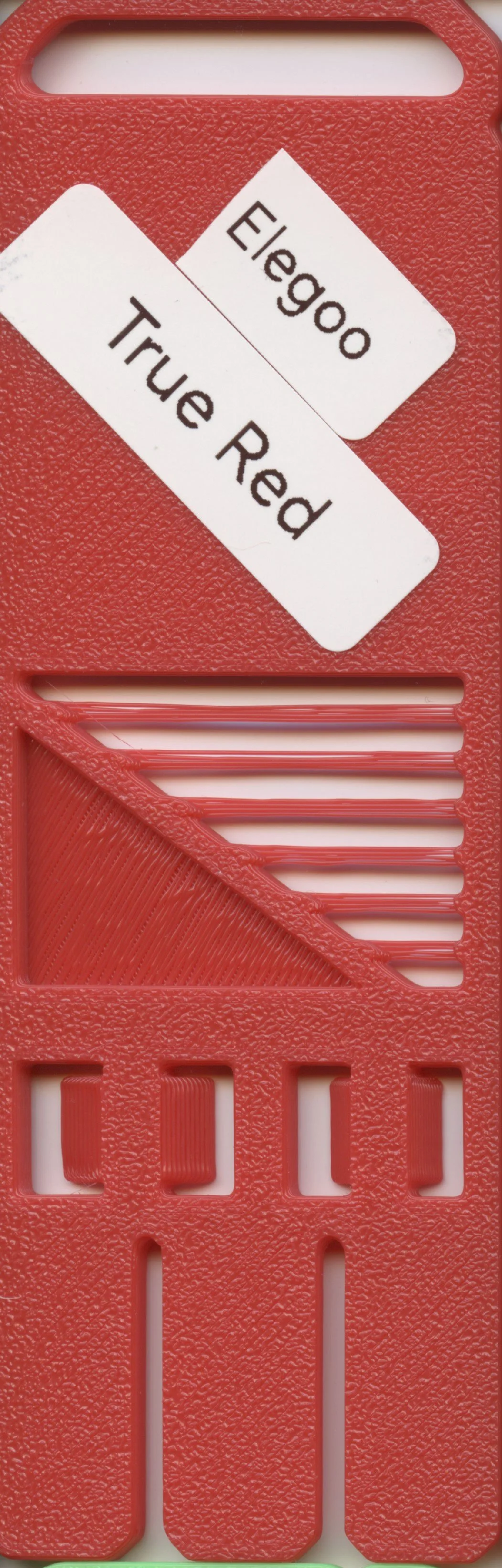 Close-up photo of a red plastic object with a textured surface, a white sticker reading 'Elegoo True Red,' and horizontal slot openings.