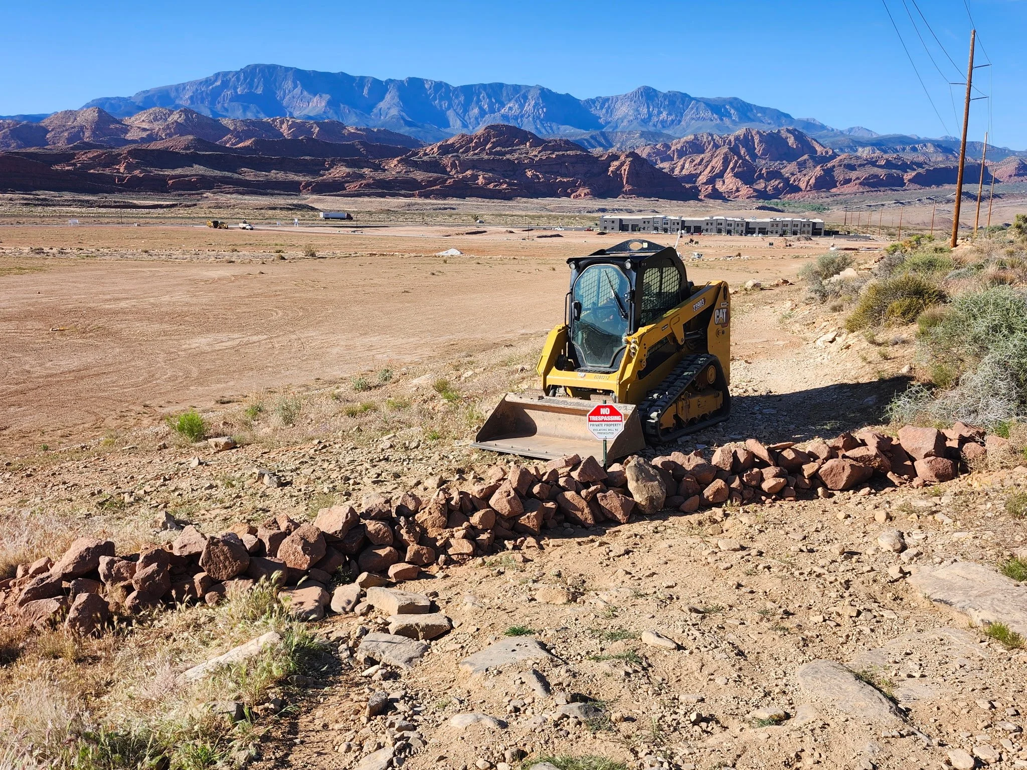 Yellow CAT compact track loader overlooking a desert construction site and rugged red-rock mountains