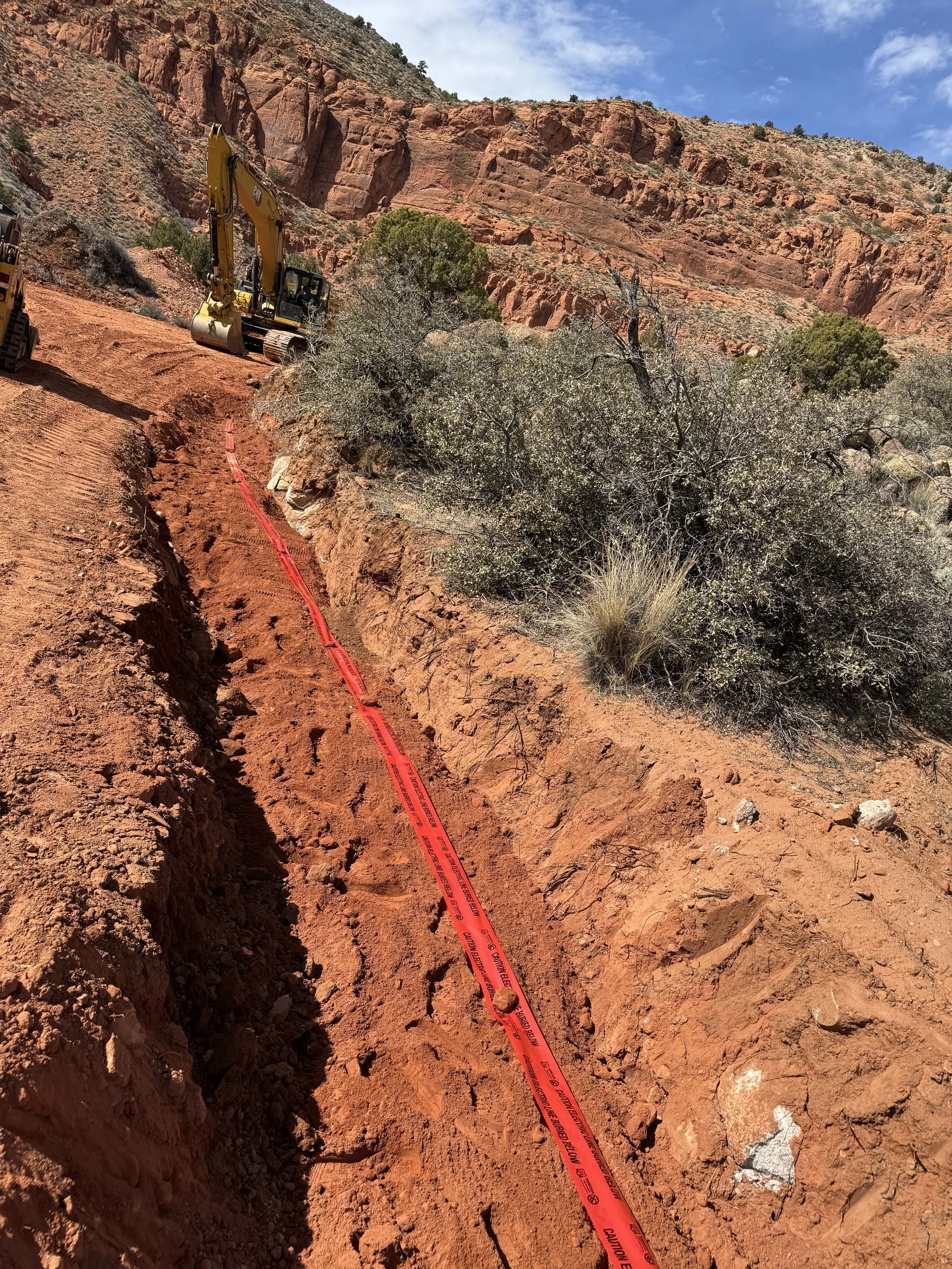Yellow excavator at a red sandstone canyon construction site with caution tape in the foreground