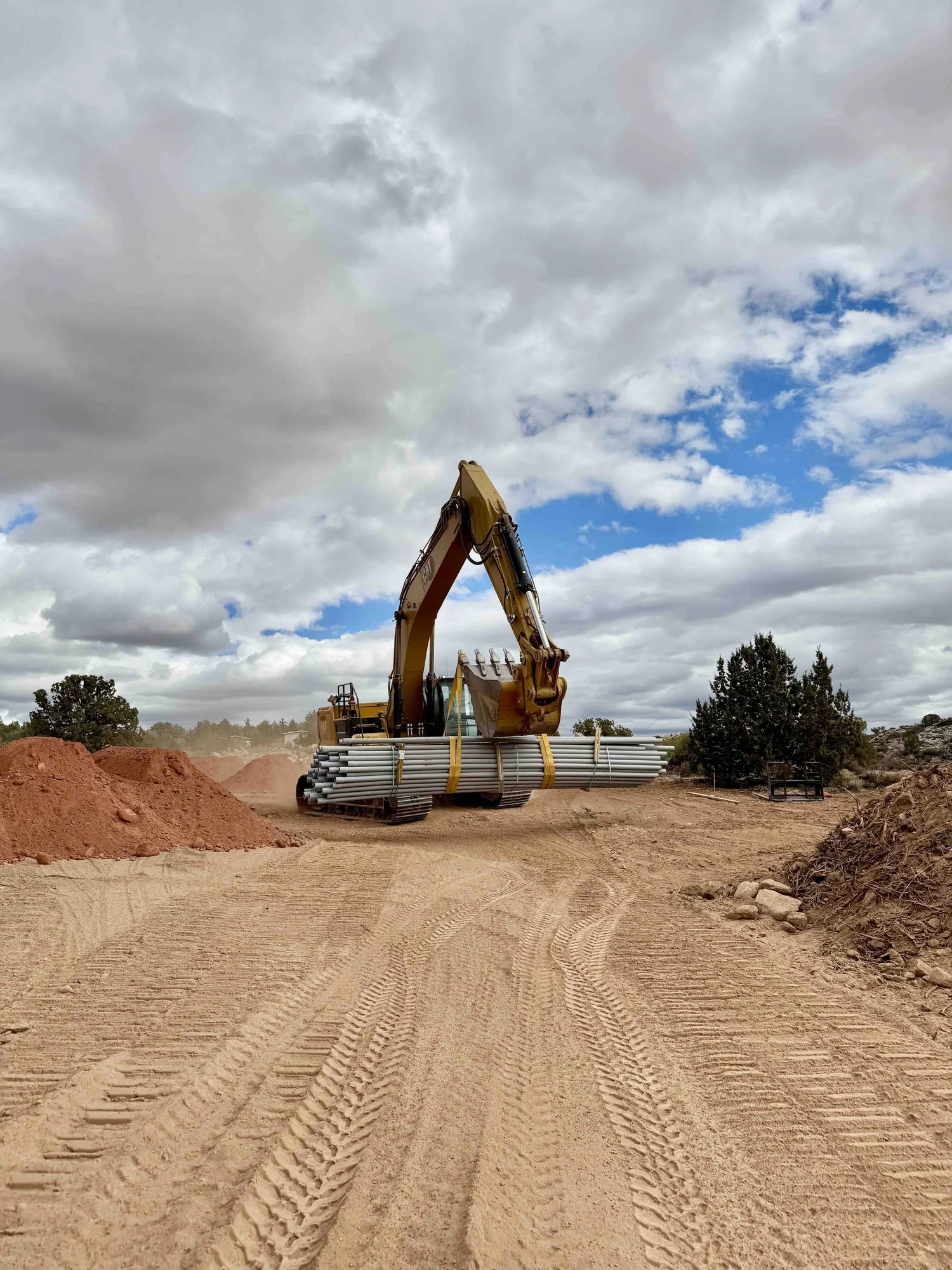 Artisan Group excavator carrying bundled underground pipe across a Southern Utah worksite