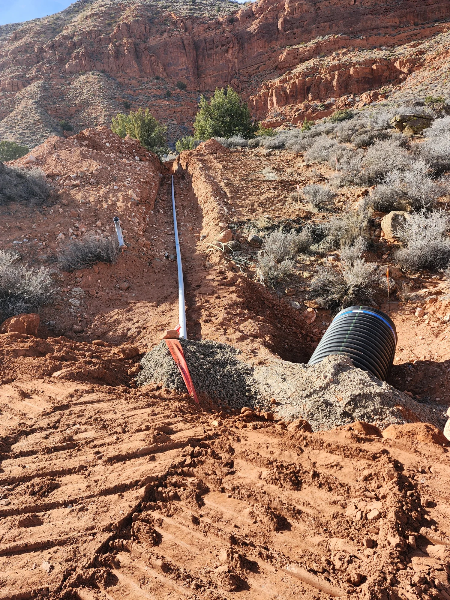 Underground pipe and corrugated culvert beside a red-soil trench amid Southern Utah rock formations