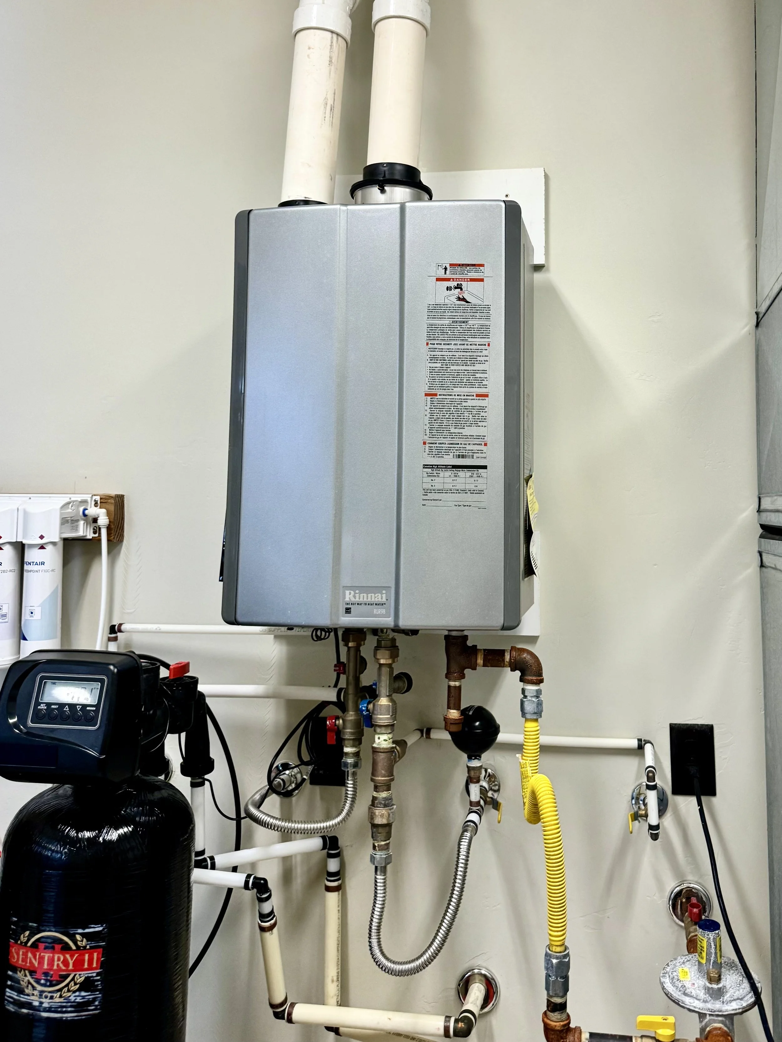 A water heater system with pipes, valves, and a control panel in a utility room.