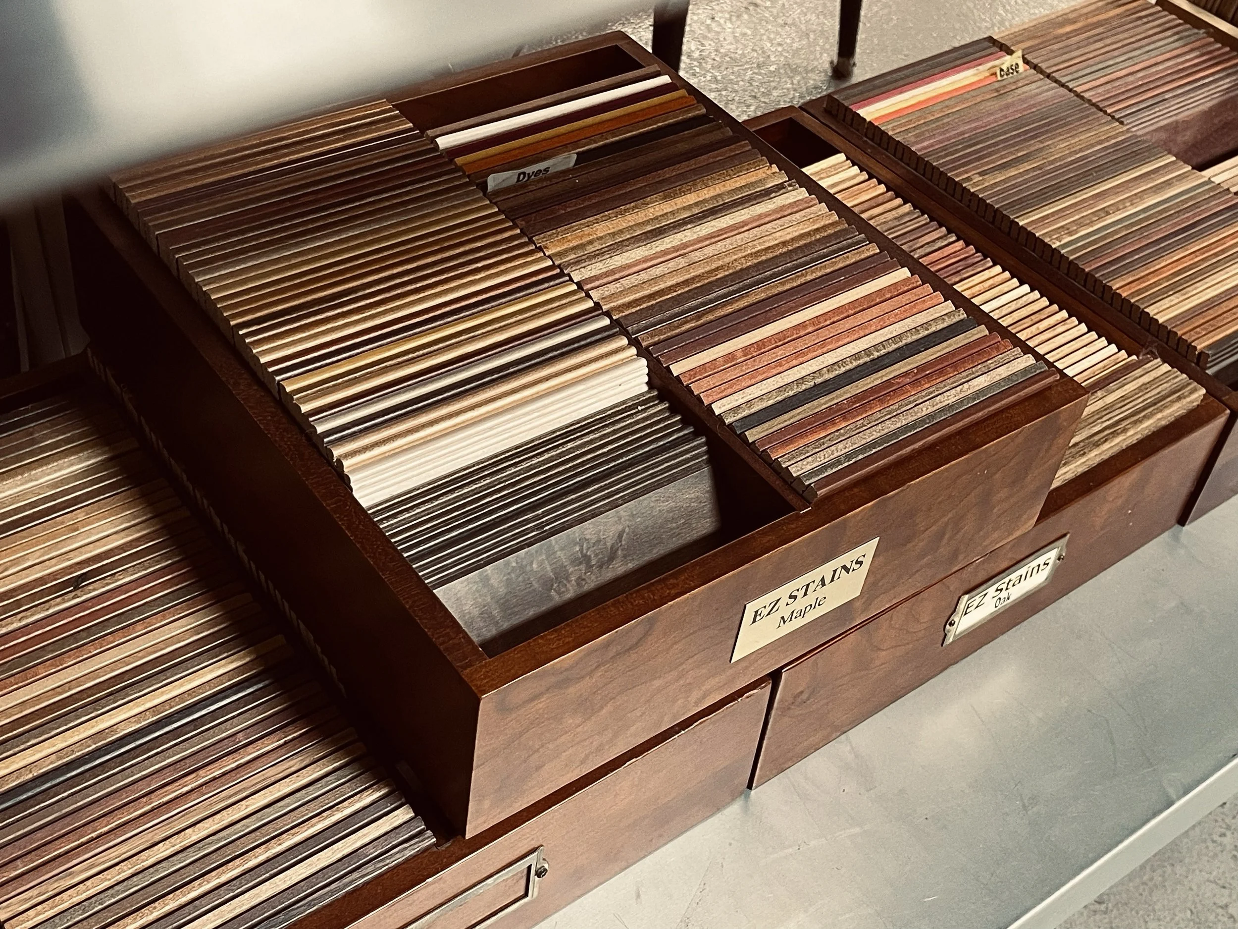 Wooden display case filled with sample wood veneer strips organized by color and type, with labels indicating wood types like 'Maple' and 'Oak'.