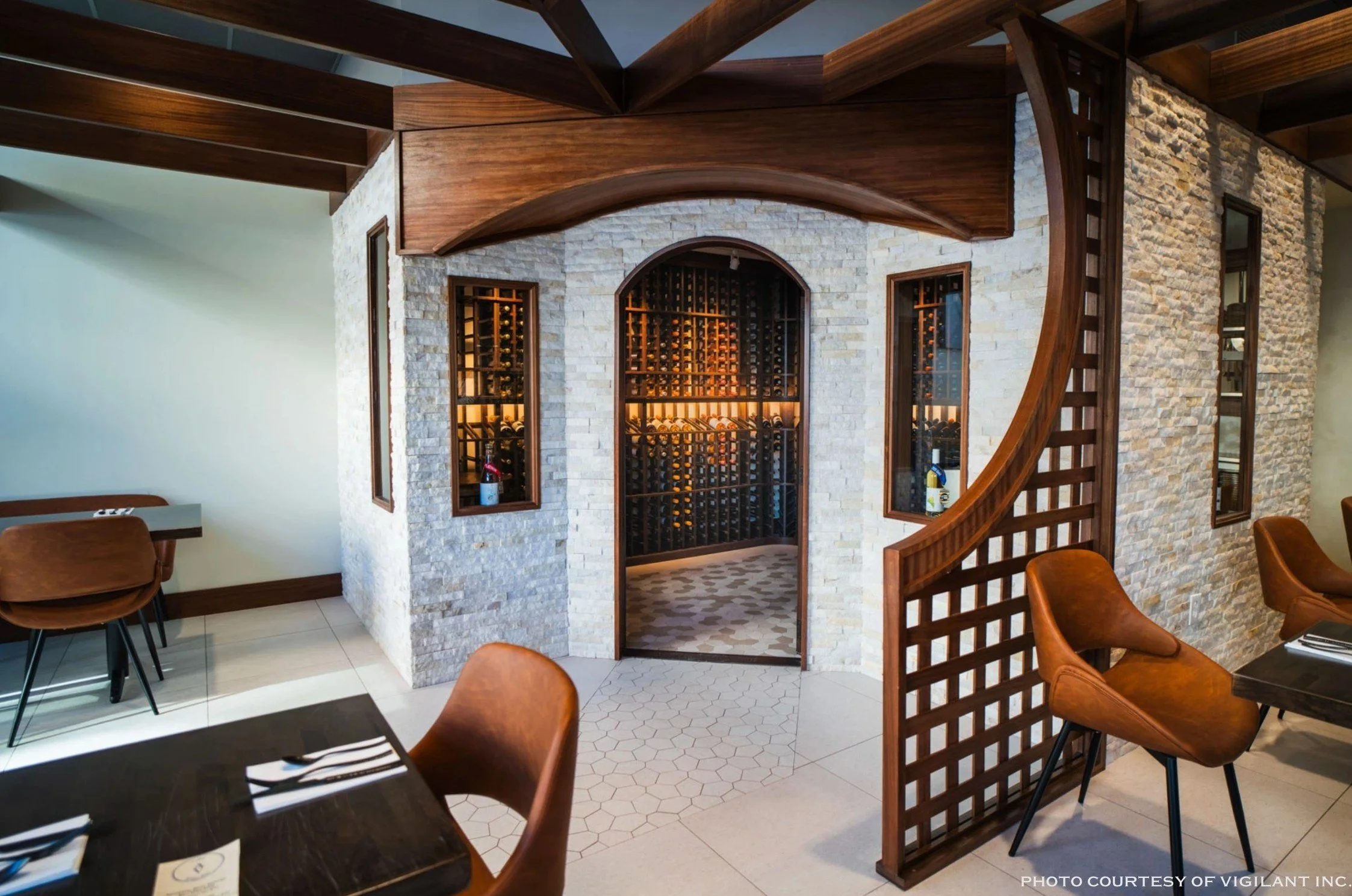 Indoor wine cellar with wooden wine racks and a stone wall. Dining tables and chairs in the foreground.