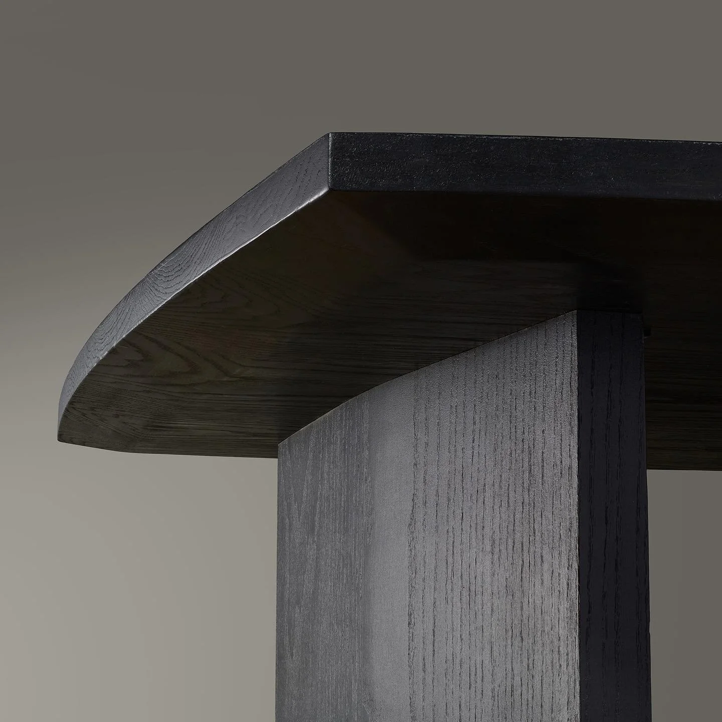 Close-up of a modern black wooden table with a curved edge, showing the texture and grain of the wood against a neutral background.