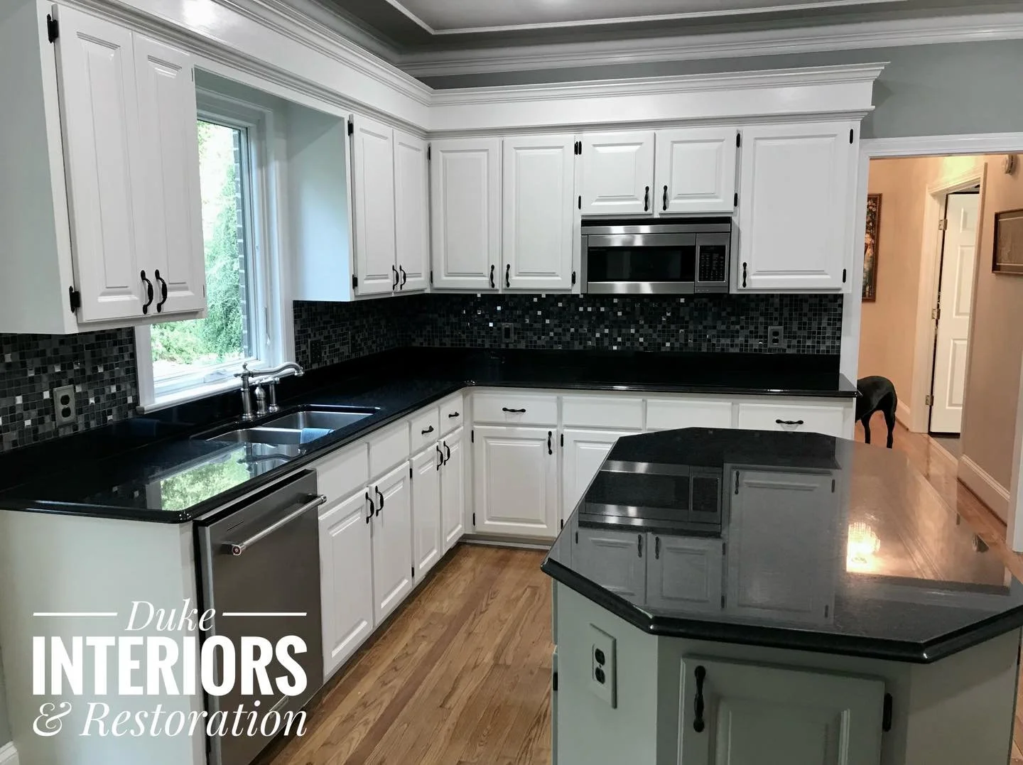 Kitchen with white cabinets, black countertops, black mosaic tile backsplash, stainless steel appliances, and hardwood floors.
