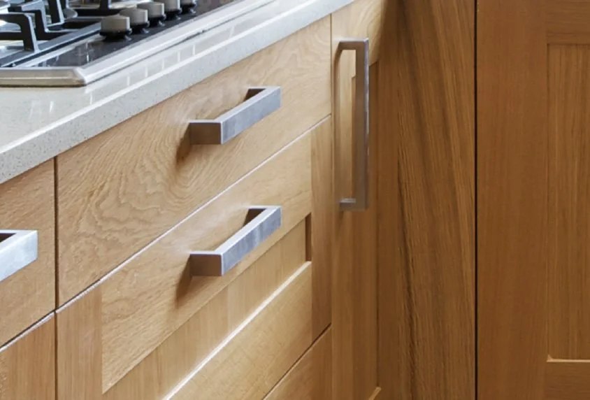 Close-up of wooden kitchen cabinets with stainless steel handles and a portion of a stove with gas burners on a light-colored countertop.