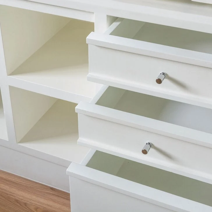 White cabinet with three drawers, each with a small metallic handle, on a wooden floor.