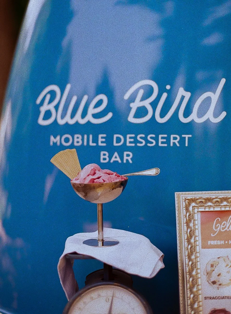 Advertisement for Blue Bird mobile dessert bar featuring a pink ice cream in a metal cup with a waffle piece, displayed on a scale with a white napkin.