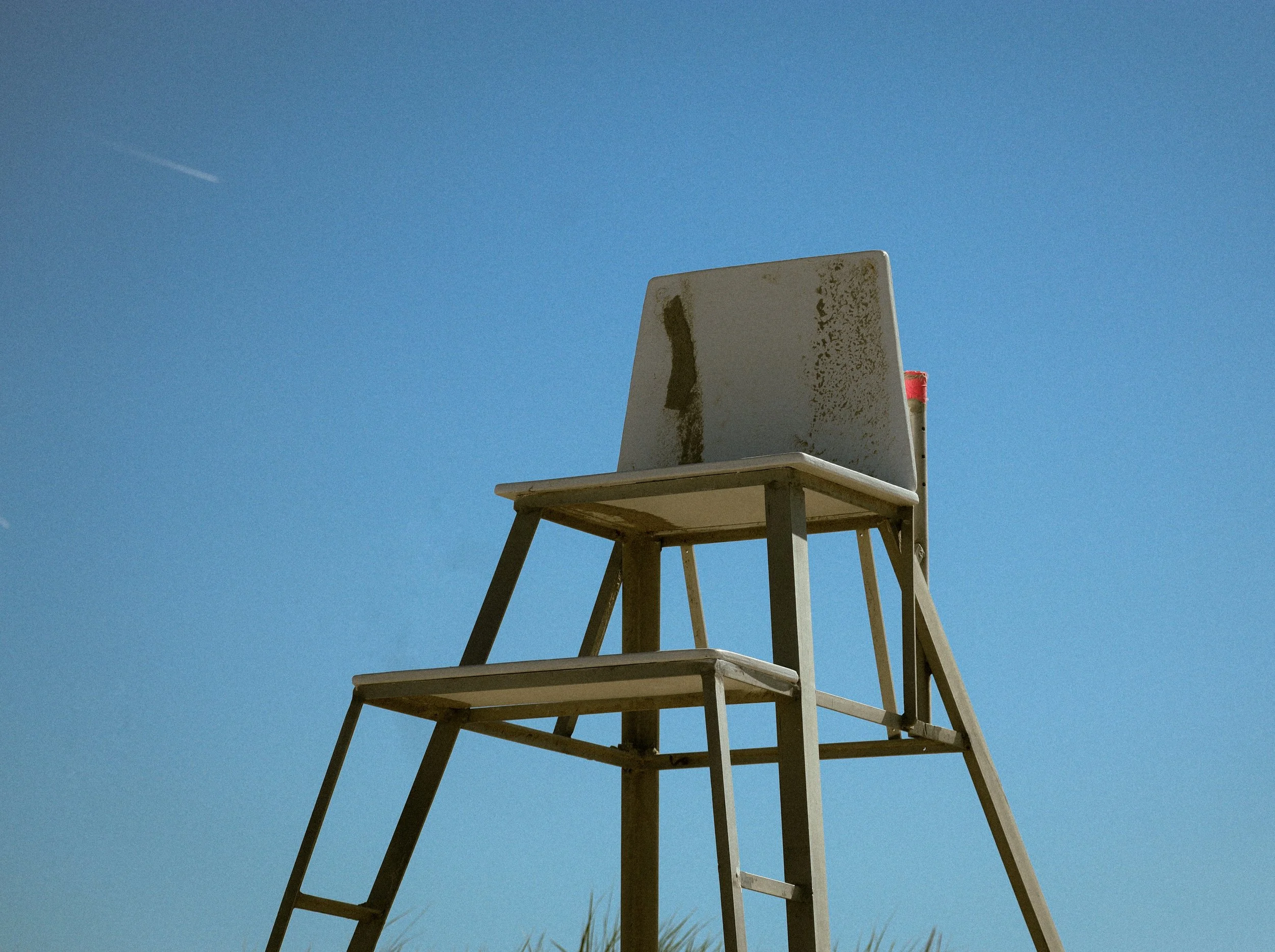 A basketball hoop with a weathered backboard and a red rim, stacked on four other matching hoops, set outdoors against a blue sky.