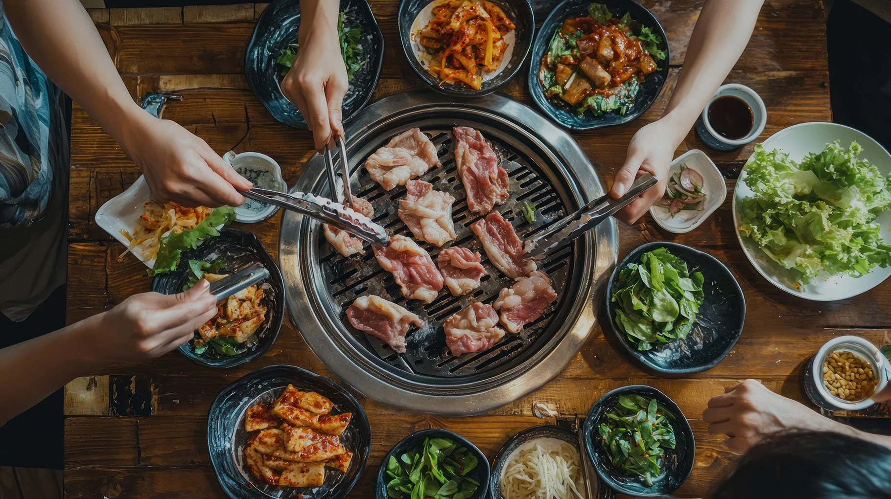 Overhead view of fresh meats cooking on a traditional table-side grill, surrounded by a colorful variety of authentic Korean banchan side dishes in Brentwood, Tennessee.